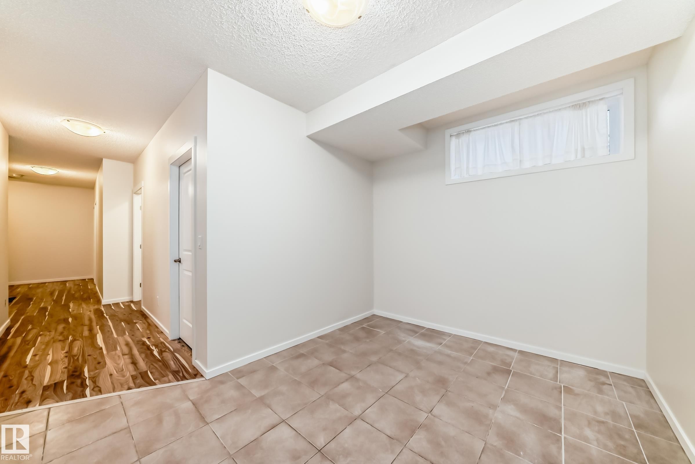 Room featuring light neutral wall paint, a small window with white trim, a textured ceiling, and large square floor tiles - 18103 77 Street, Edmonton, AB