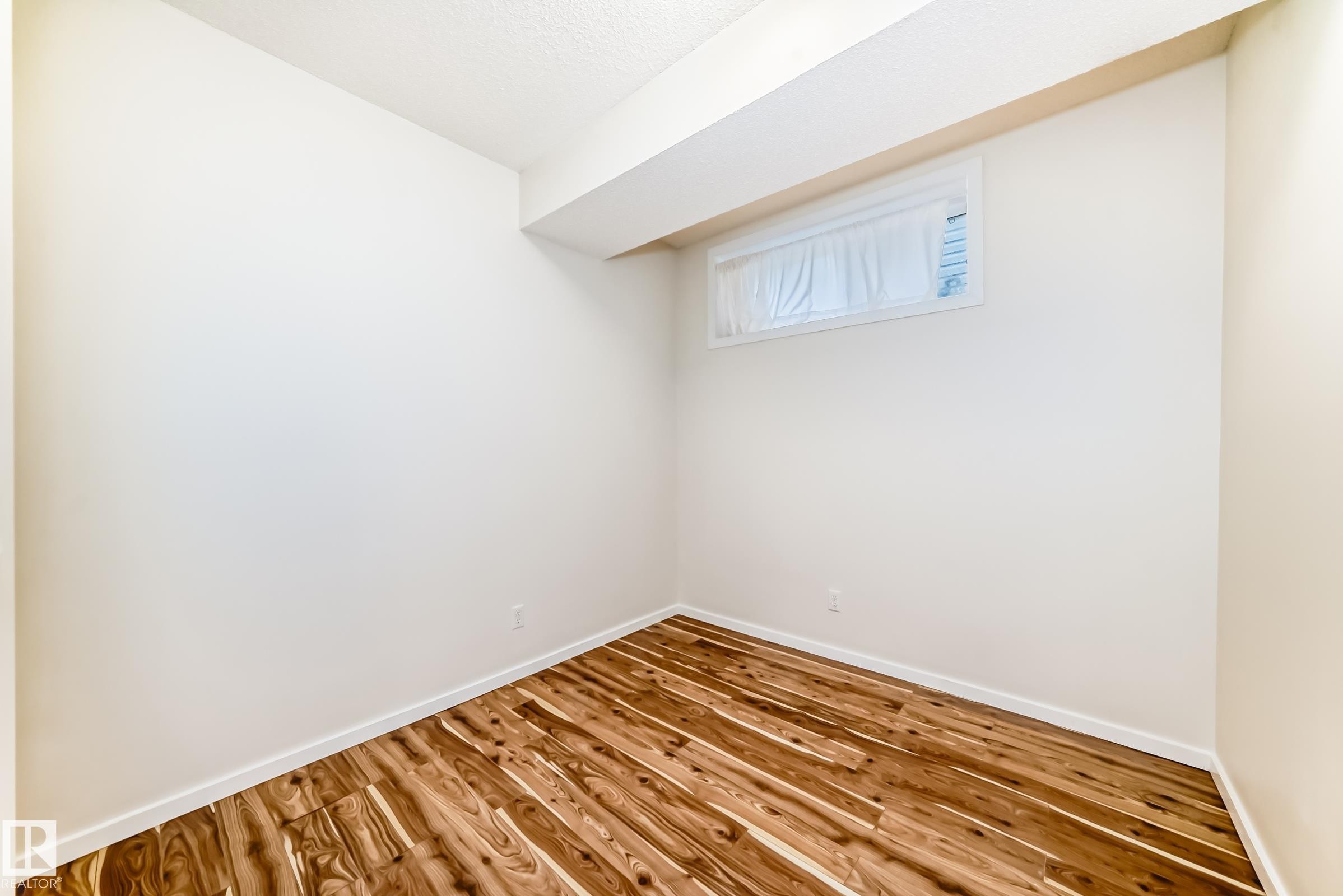 Room featuring wood-finish flooring, white baseboards, and a window with a sheer covering - 18103 77 Street, Edmonton, AB