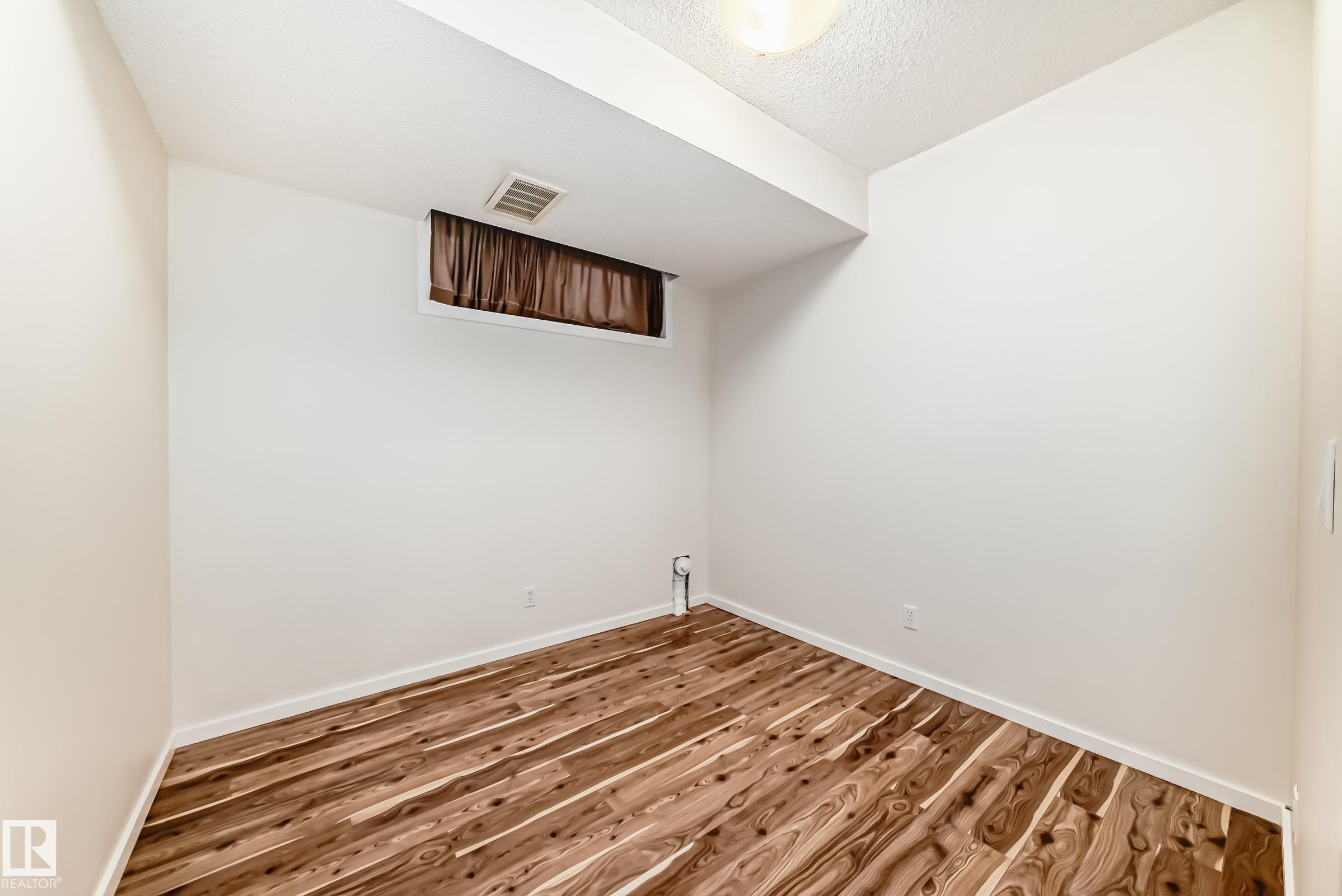 Room featuring wood-finish flooring, white baseboards, and a window with brown drapes - 18103 77 Street, Edmonton, AB