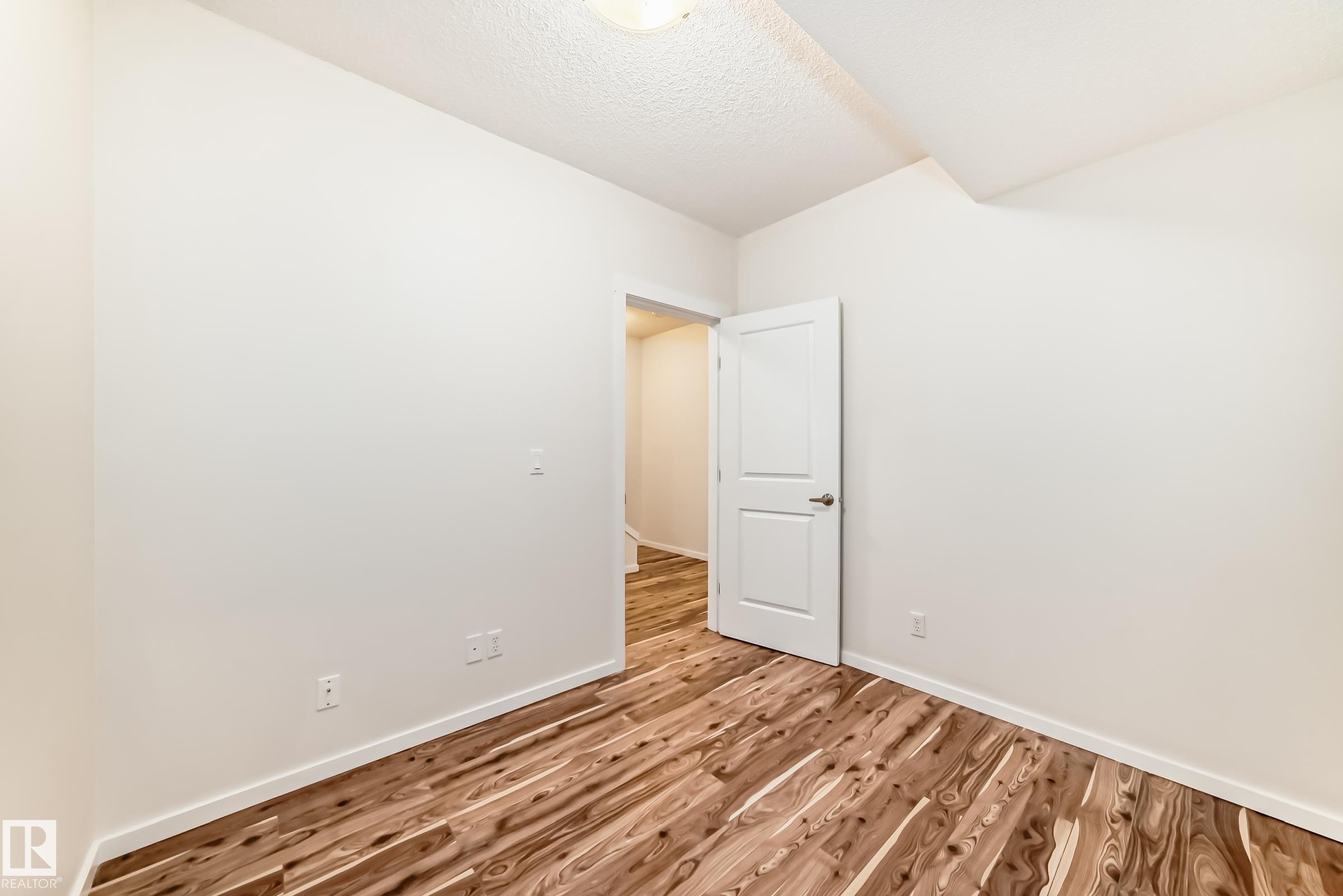 Room featuring wood-finish flooring, white baseboards, and a white interior door with a silver-tone handle - 18103 77 Street, Edmonton, AB