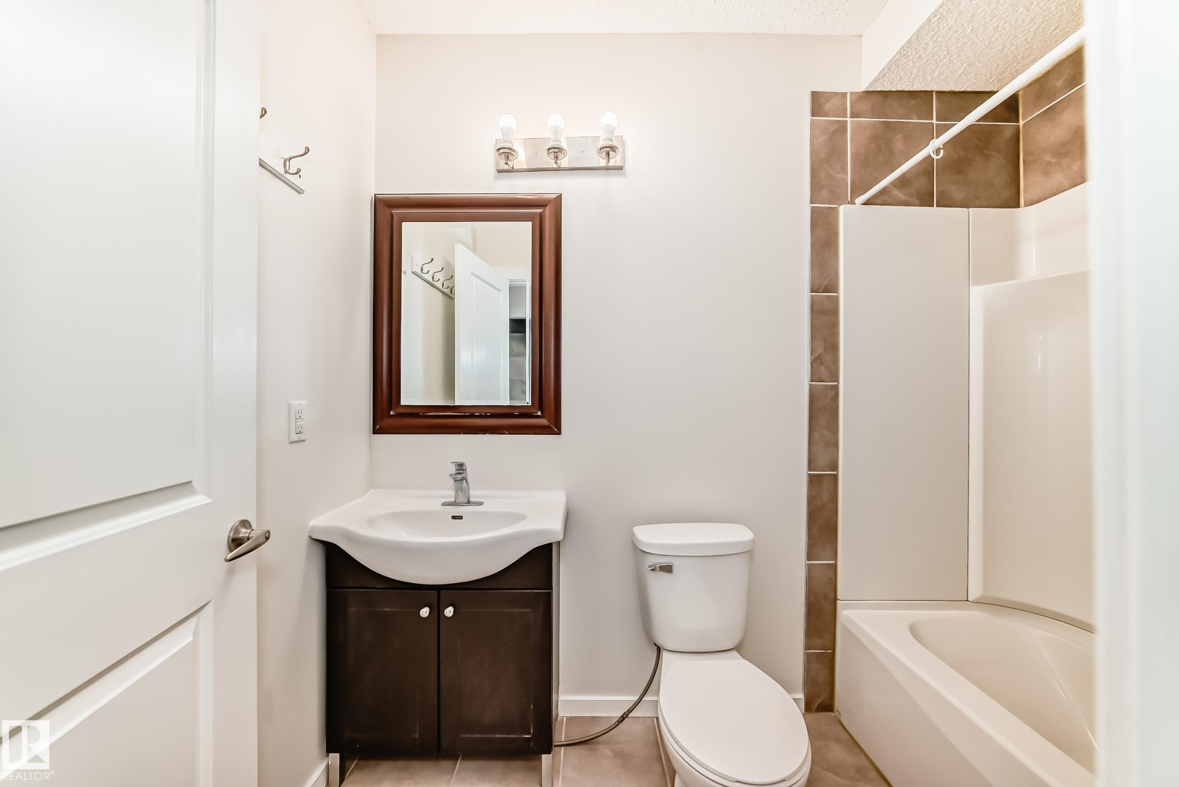 Bathroom featuring a white vanity with integrated sink, dark wood-finish cabinet, and a framed mirror - 18103 77 Street, Edmonton, AB