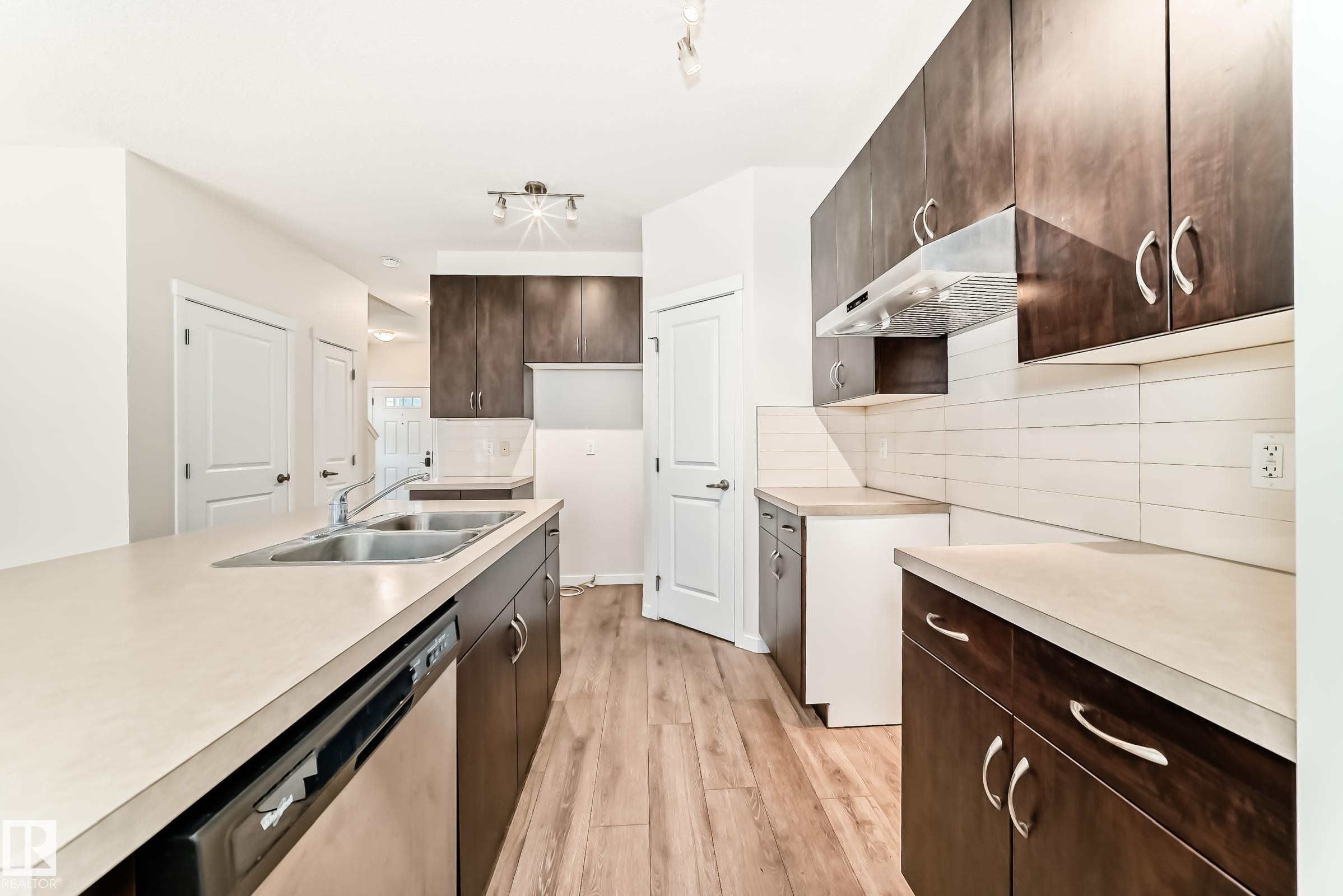 Kitchen featuring wood-finish flooring, dark wood cabinetry, light-toned countertops, and a subway tile backsplash - 18103 77 Street, Edmonton, AB