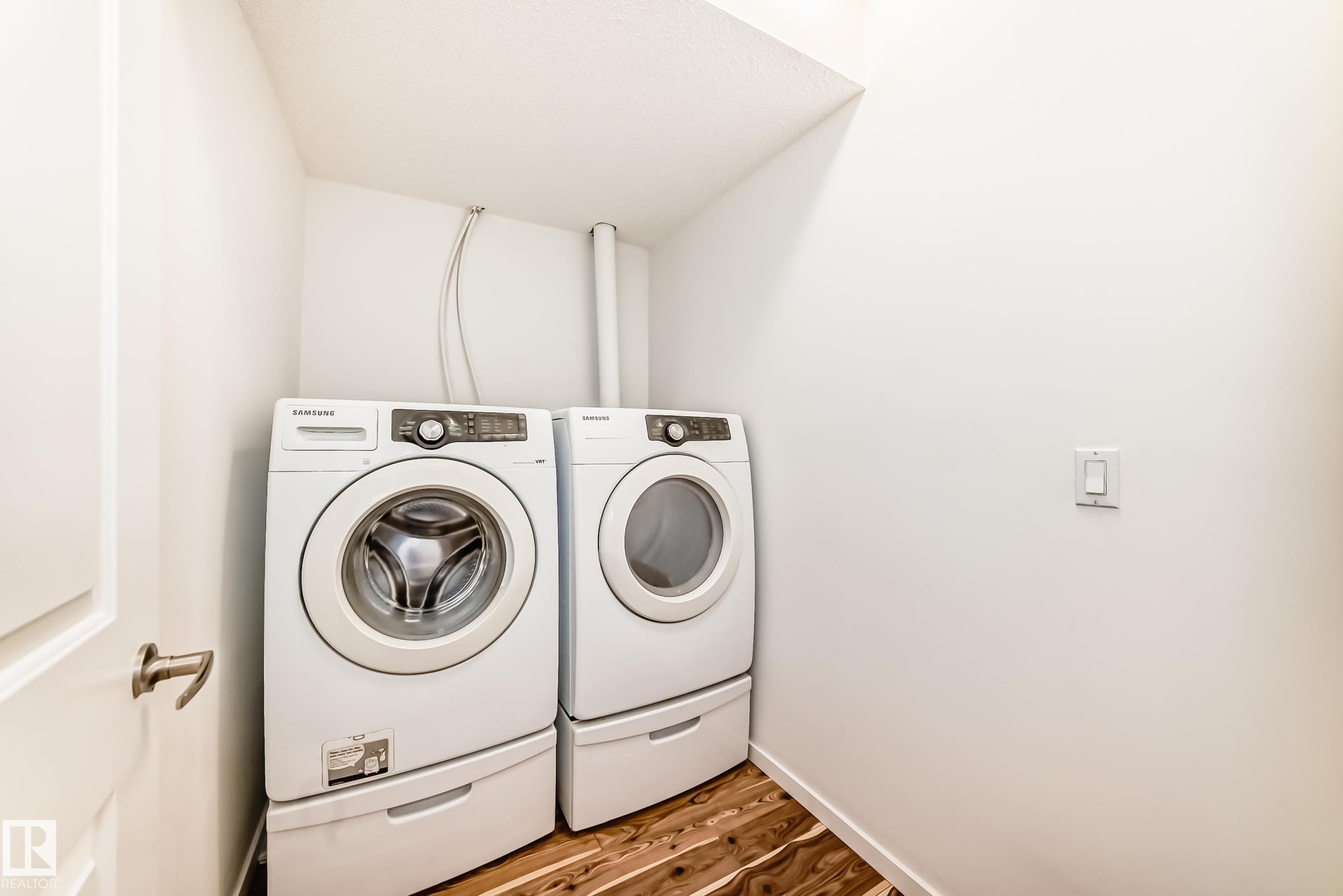 Dedicated laundry area featuring wood-finish flooring, white walls, and a light switch with a white cover plate - 18103 77 Street, Edmonton, AB