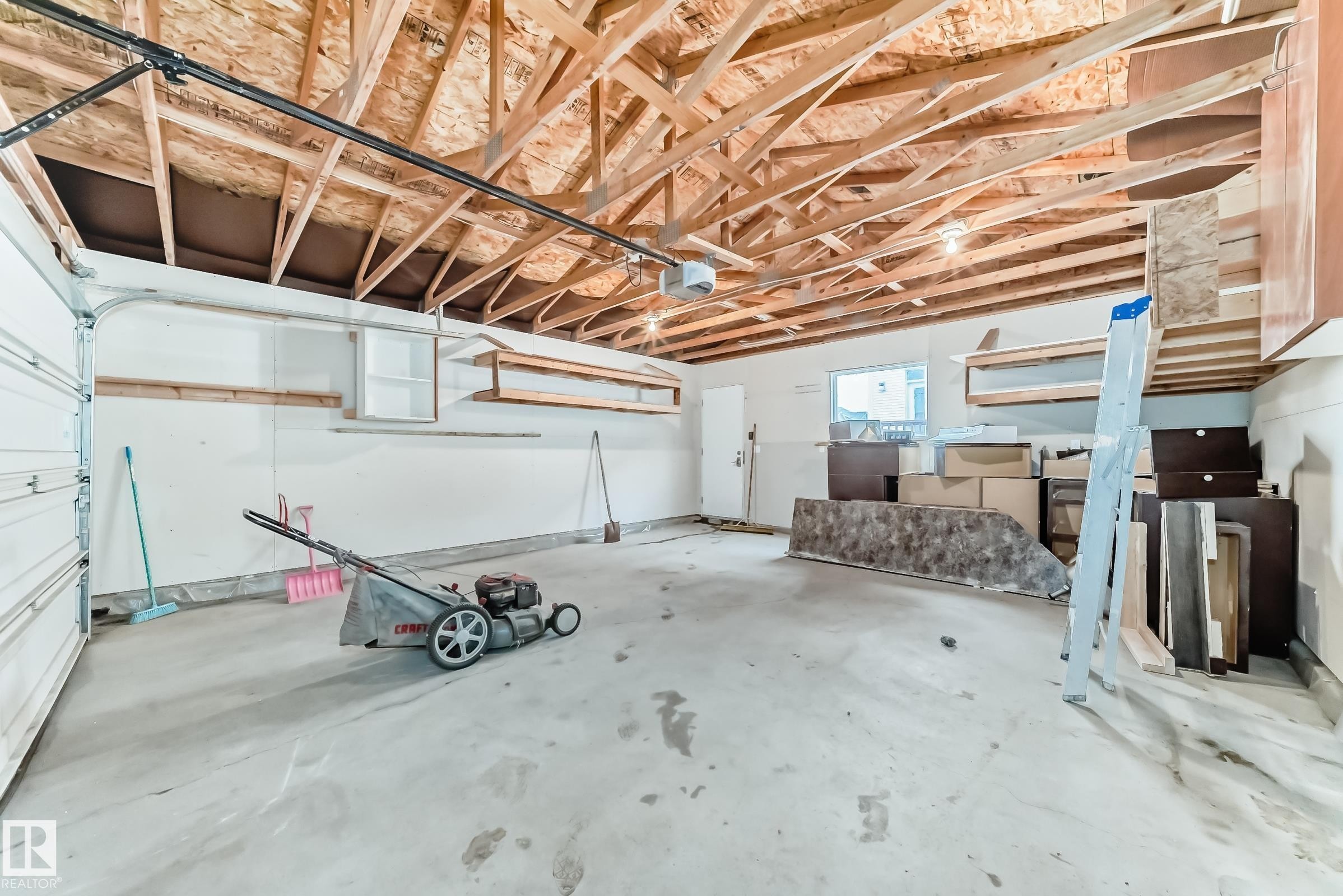 Spacious garage with exposed wood ceiling beams, concrete flooring, and an overhead garage door - 18103 77 Street, Edmonton, AB