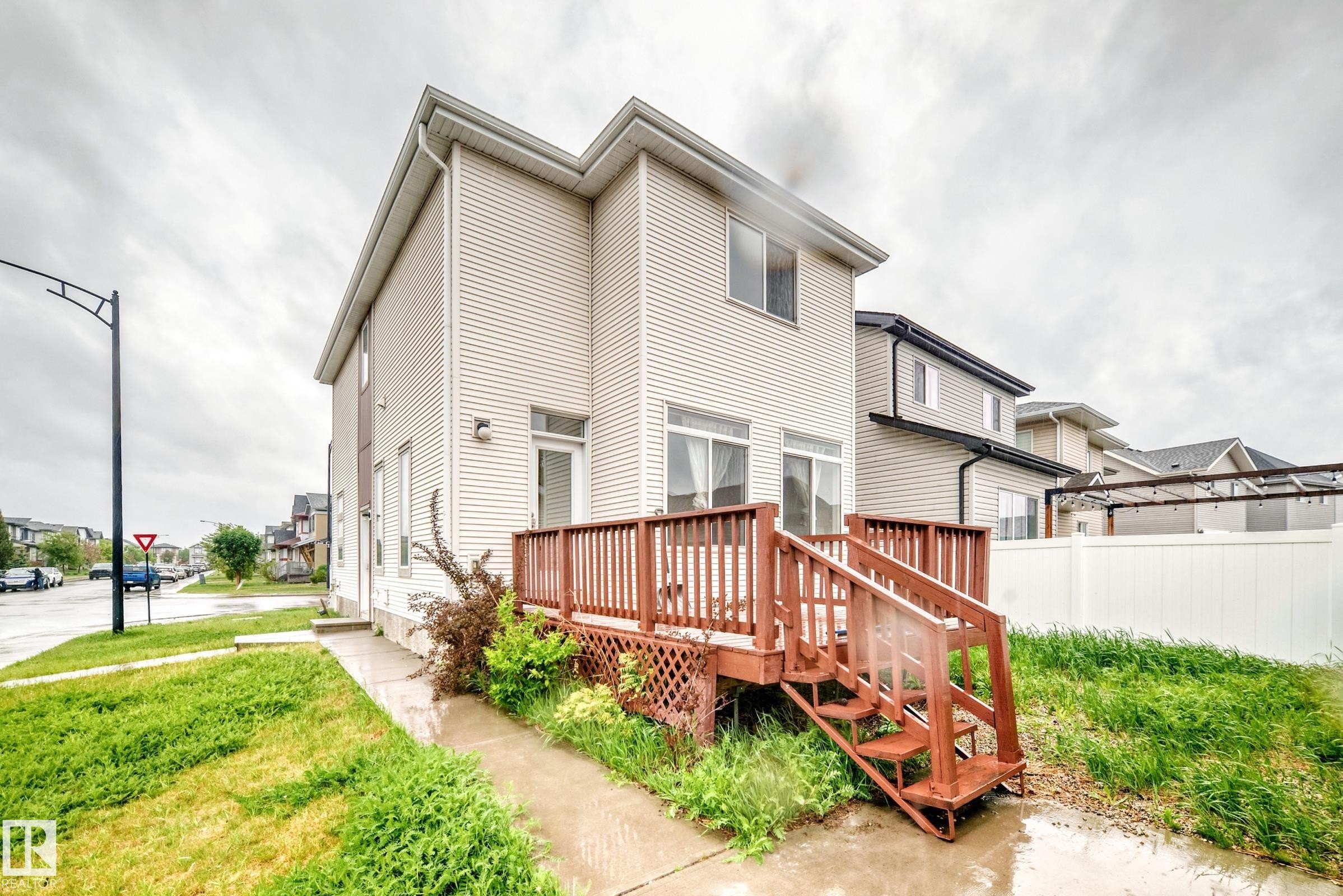 Rear exterior featuring a wooden deck with railing and stairs, vinyl siding, sliding glass doors, and a white privacy fence - 18103 77 Street, Edmonton, AB