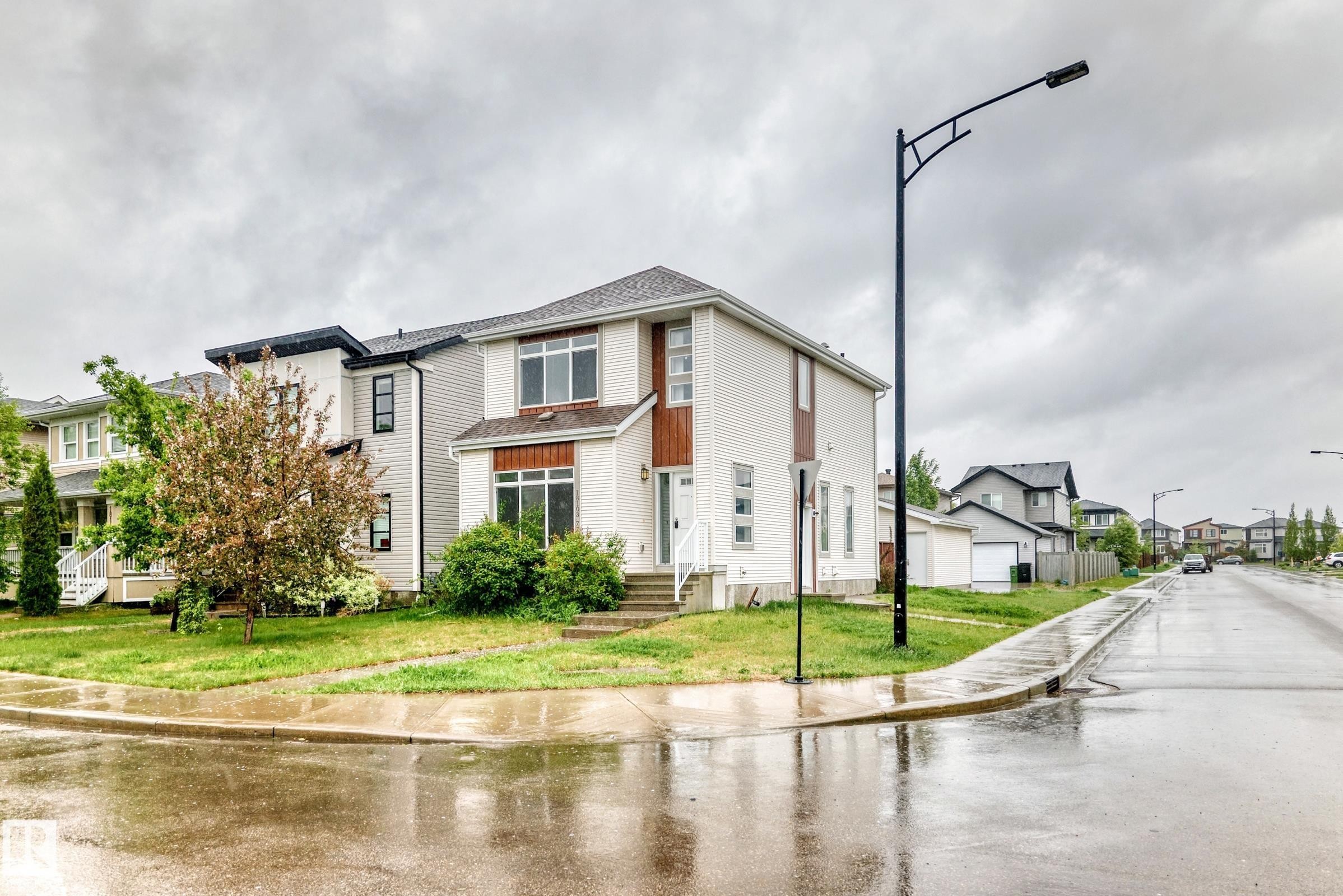 Contemporary two-story residence featuring light-colored siding, a dark shingle roof, and wood-finish accent panels - 18103 77 Street, Edmonton, AB