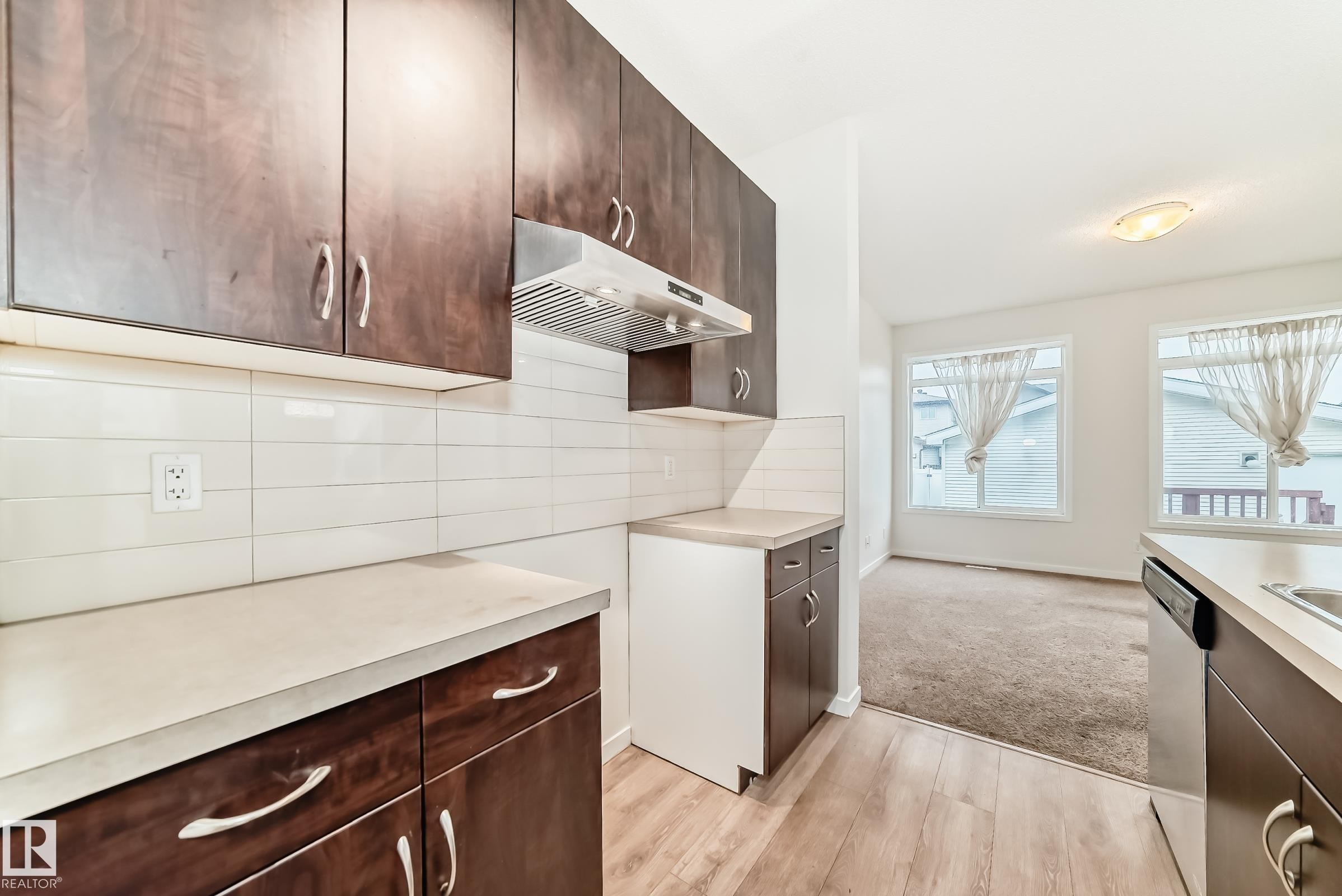 Kitchen featuring wood-finish flooring, dark wood cabinetry, light-toned countertops, and a white subway tile backsplash - 18103 77 Street, Edmonton, AB