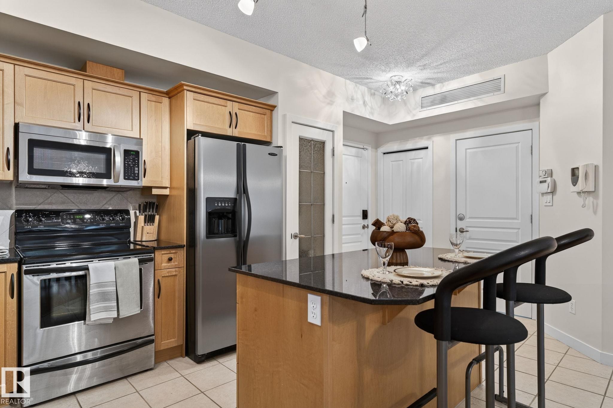 Kitchen featuring wood cabinetry, stainless steel appliances, a tile backsplash, and a breakfast bar with a dark countertop - 208 5 Gate Avenue, St. Albert, AB