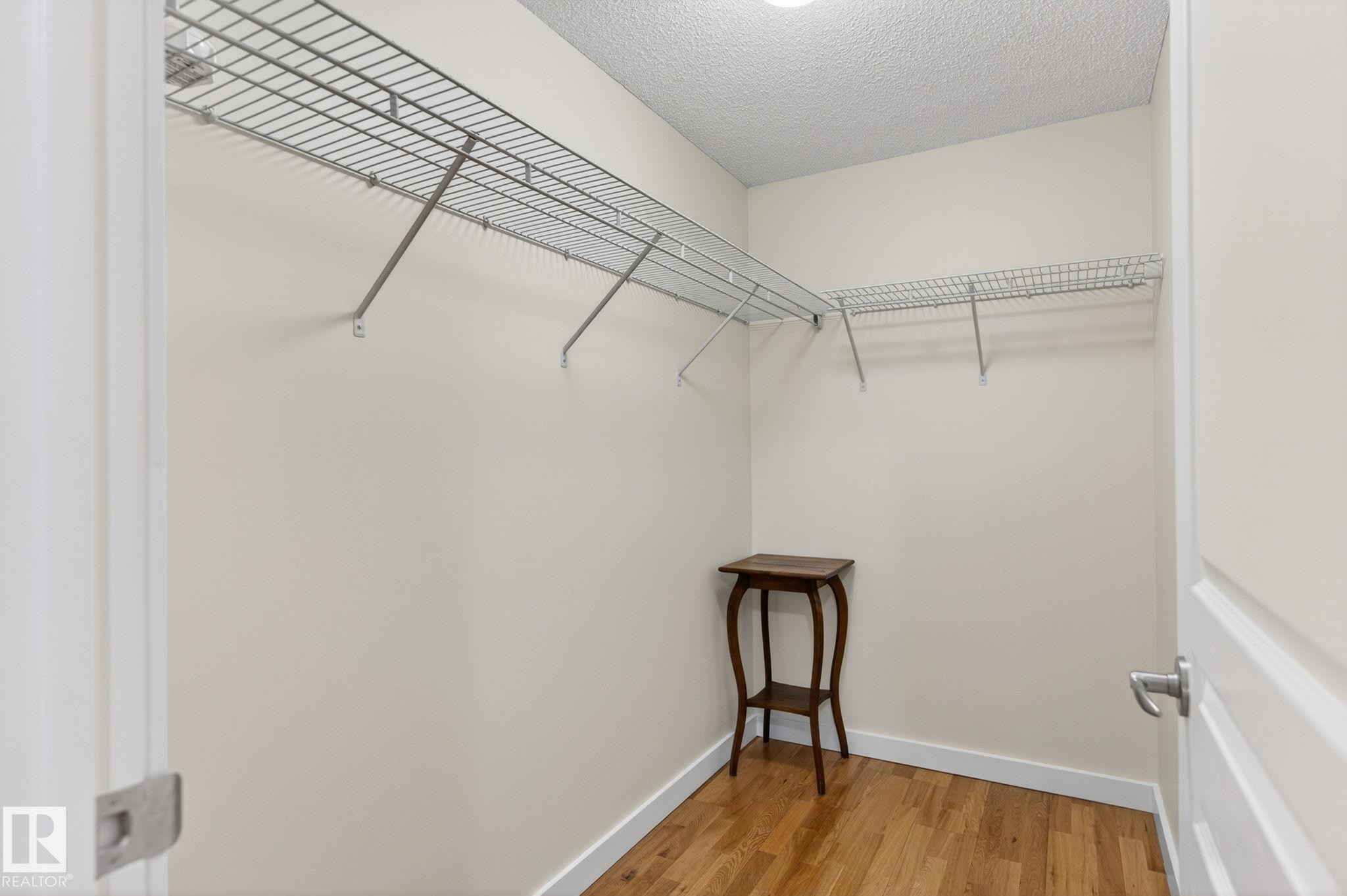 Spacious closet featuring built-in wire shelving, warm wood-finish flooring, and white baseboards - 208 5 Gate Avenue, St. Albert, AB