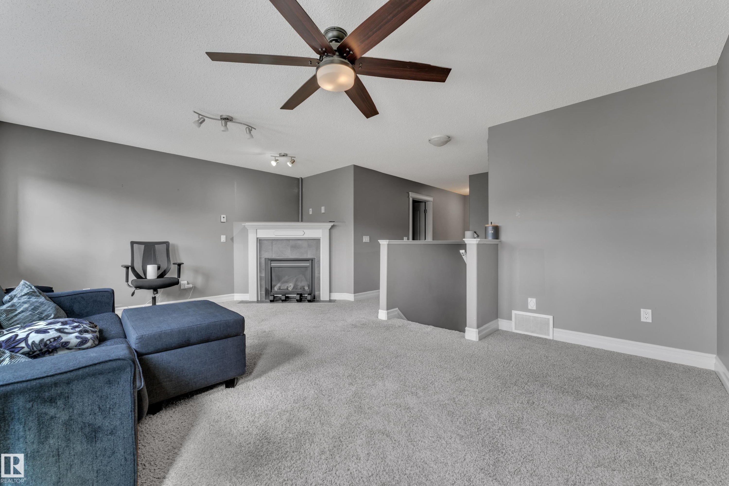 Spacious living area featuring a fireplace with a white mantel, overhead ceiling fan with lighting, recessed lighting, carpet flooring, and a half-wall partition - 6116 11 Avenue, Edmonton, AB
