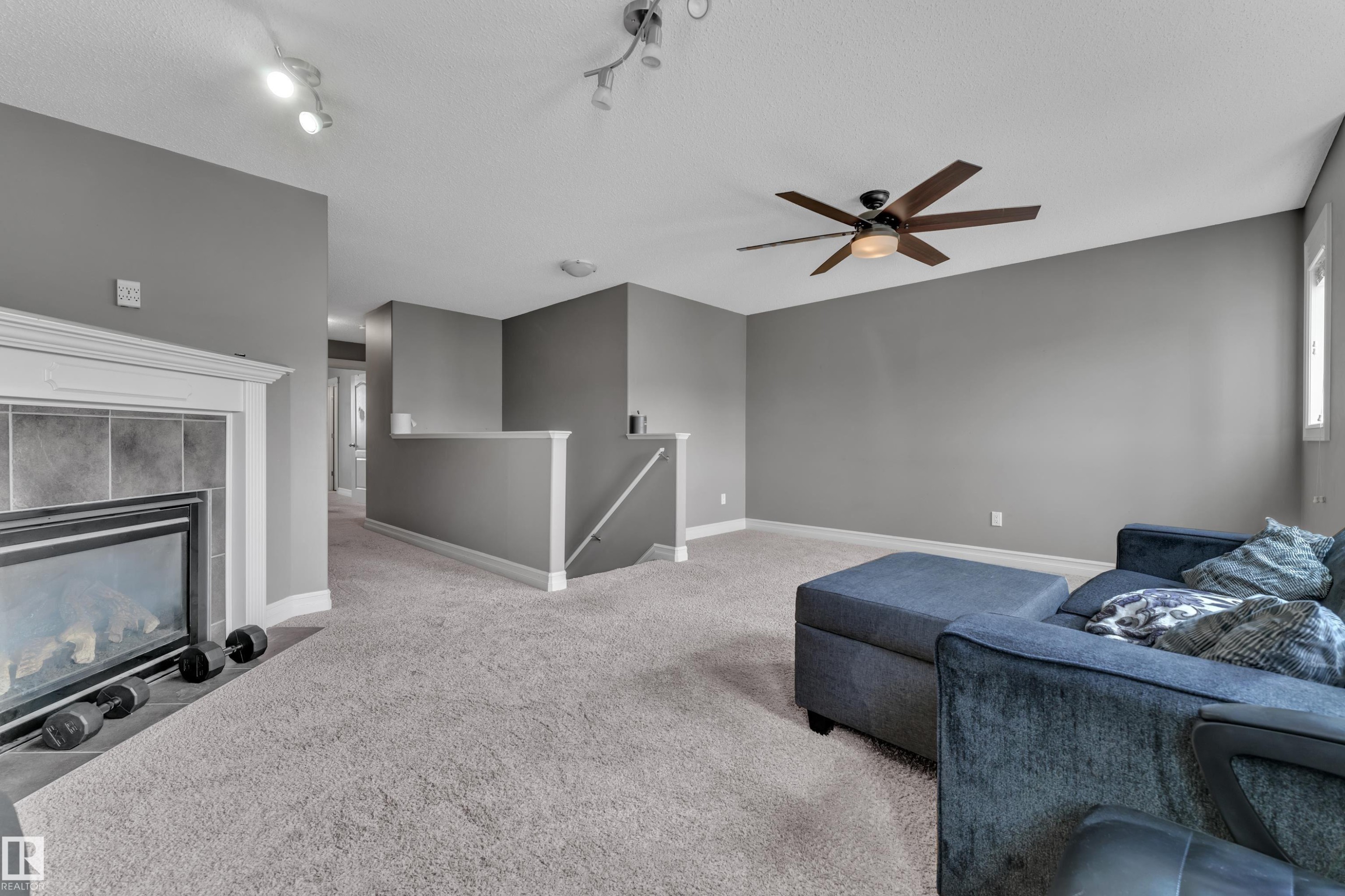 Carpeted living space featuring a fireplace with a tile surround and white mantel, a ceiling fan with light fixture, and track lighting - 6116 11 Avenue, Edmonton, AB