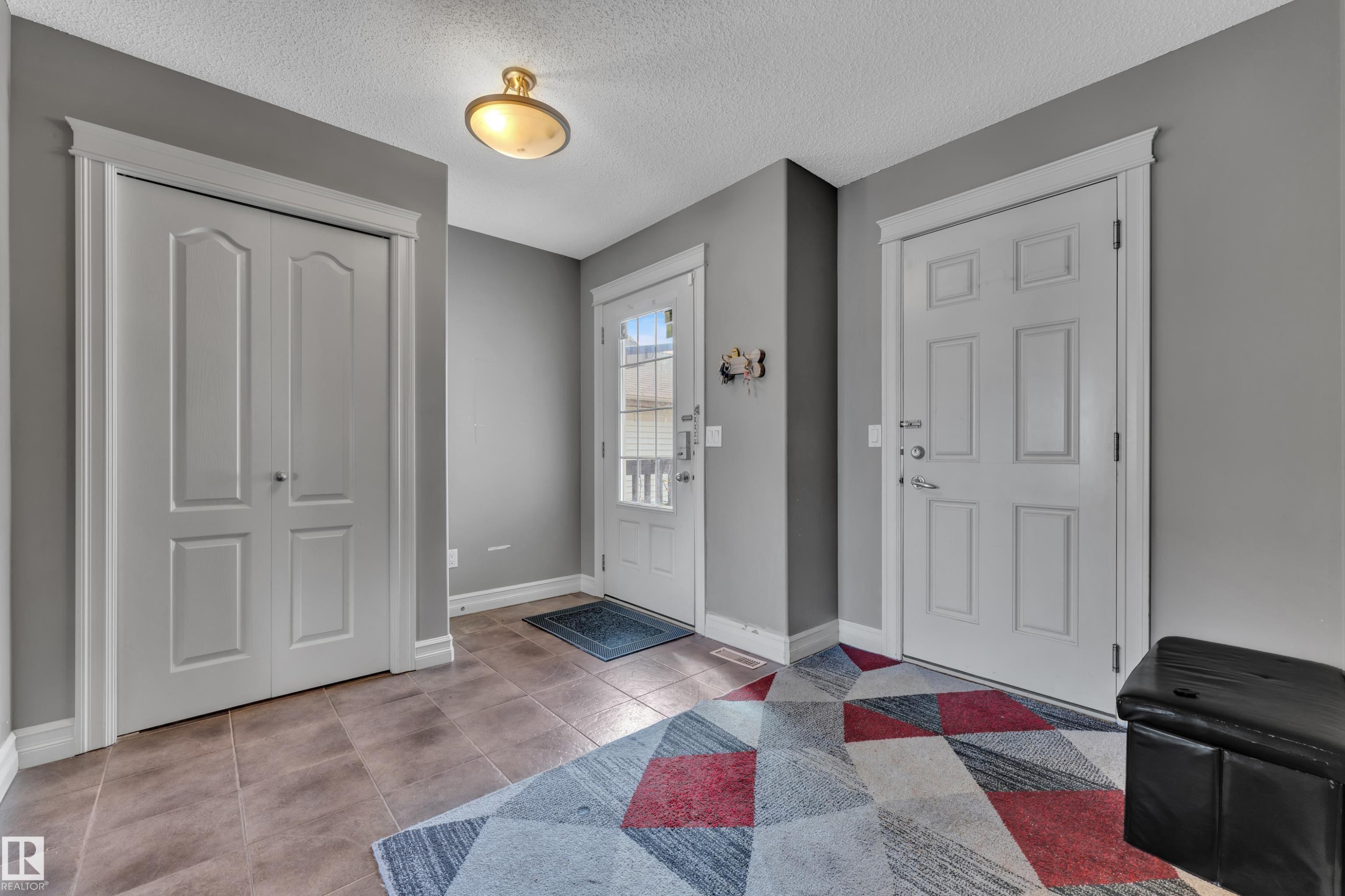 Entryway featuring tile flooring, a prominent overhead light fixture, white trim, and a white paneled door with window accents - 6116 11 Avenue, Edmonton, AB
