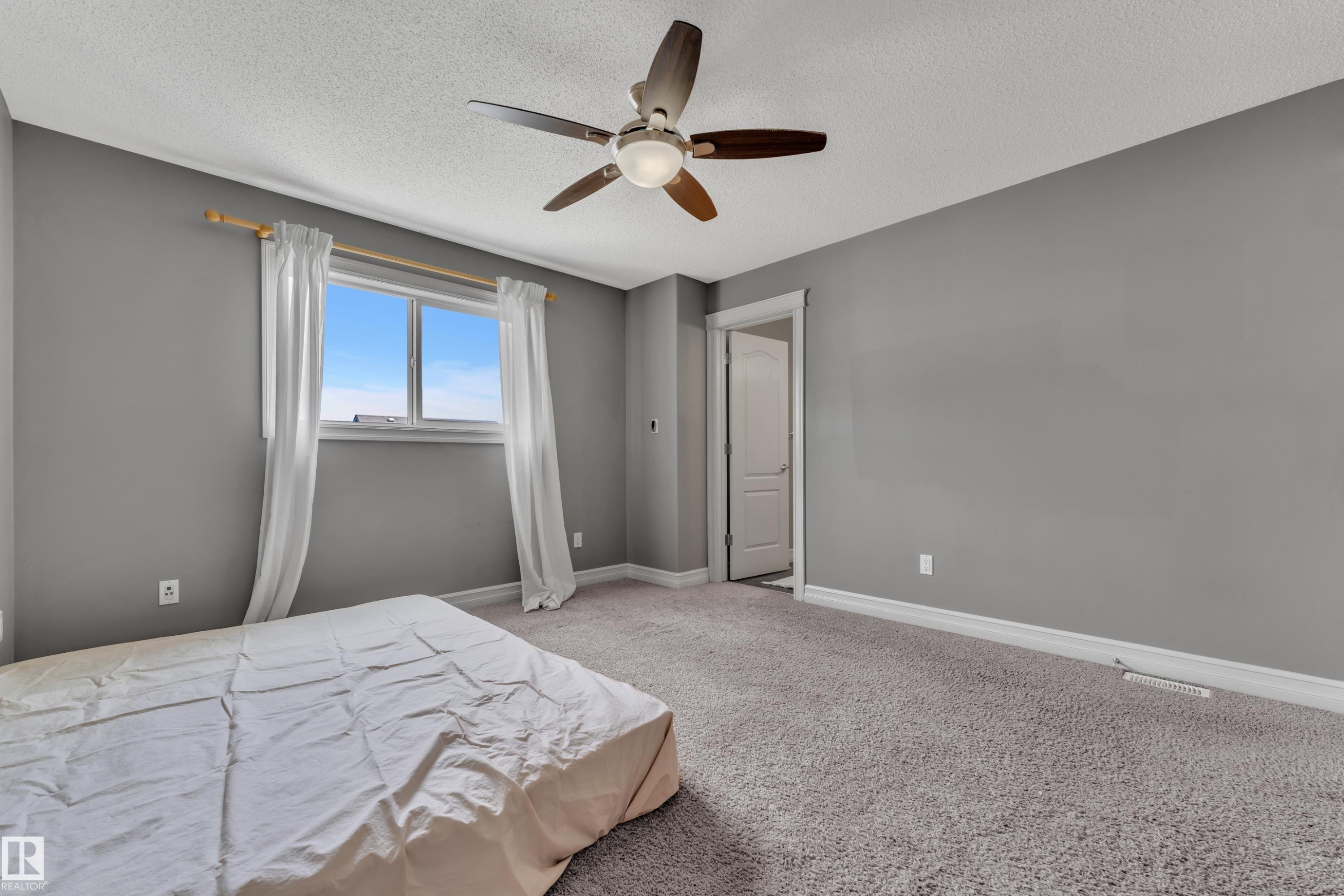Carpeted room featuring a ceiling fan with light fixture, window with natural light, and a white interior door with trim - 6116 11 Avenue, Edmonton, AB