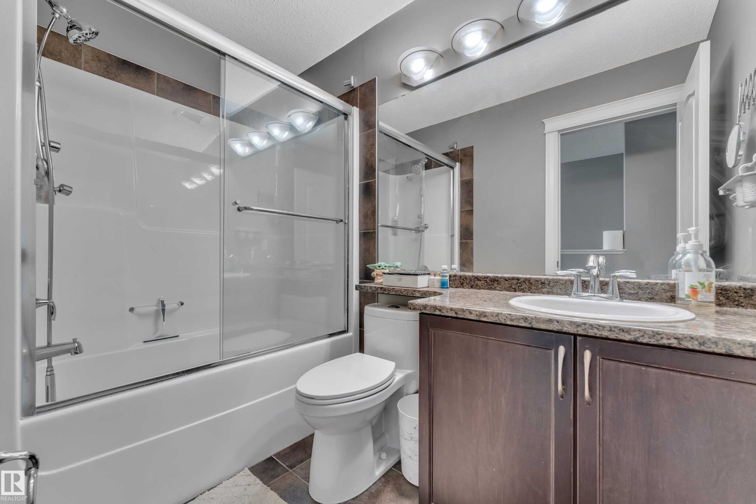 Full bathroom featuring a shower-tub combination with sliding glass doors, a vanity with wood-finish cabinetry, an oval sink, and a speckled countertop - 6116 11 Avenue, Edmonton, AB