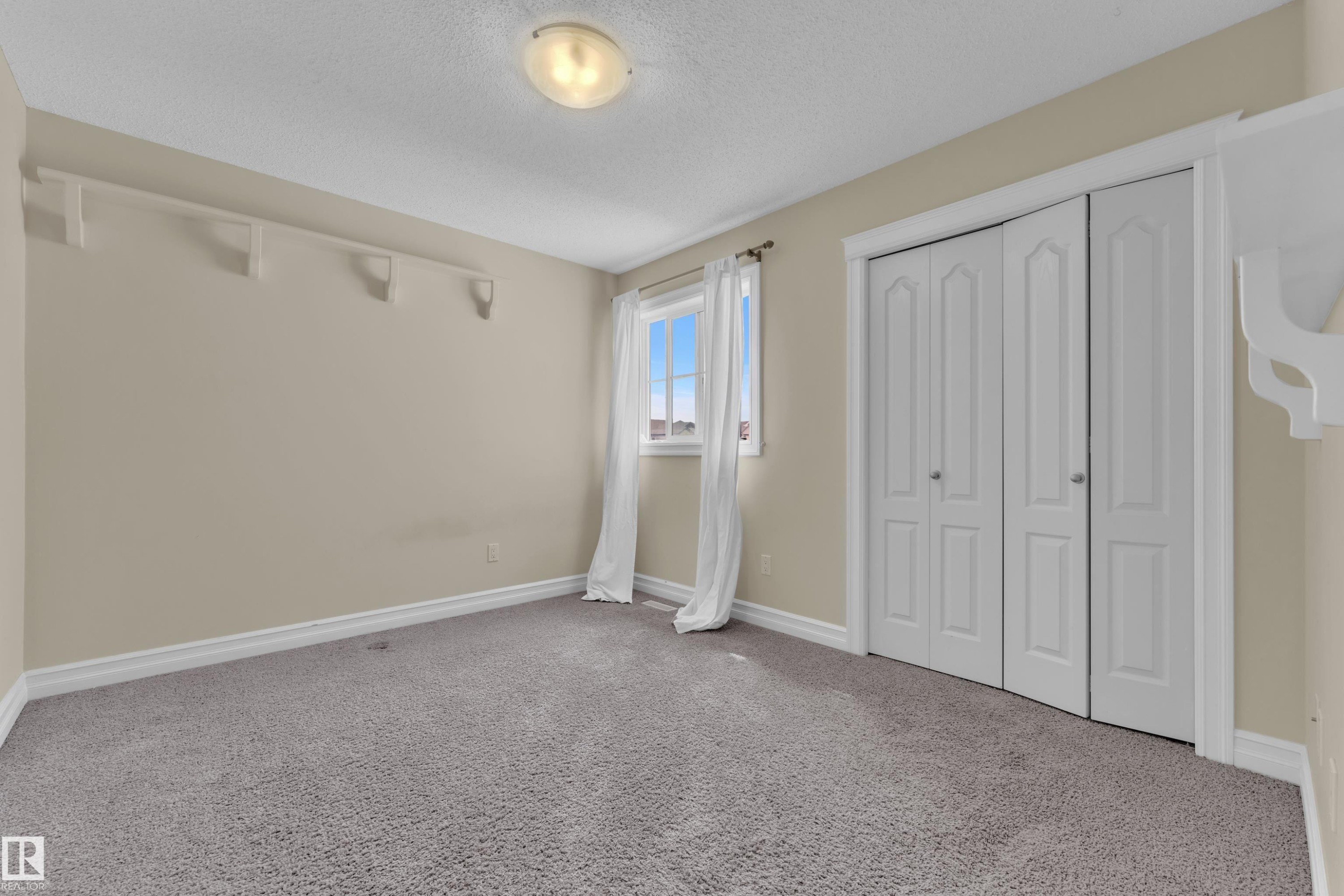 Carpeted room featuring a single window with white trim, a flush-mount ceiling light, and bi-fold closet doors - 6116 11 Avenue, Edmonton, AB