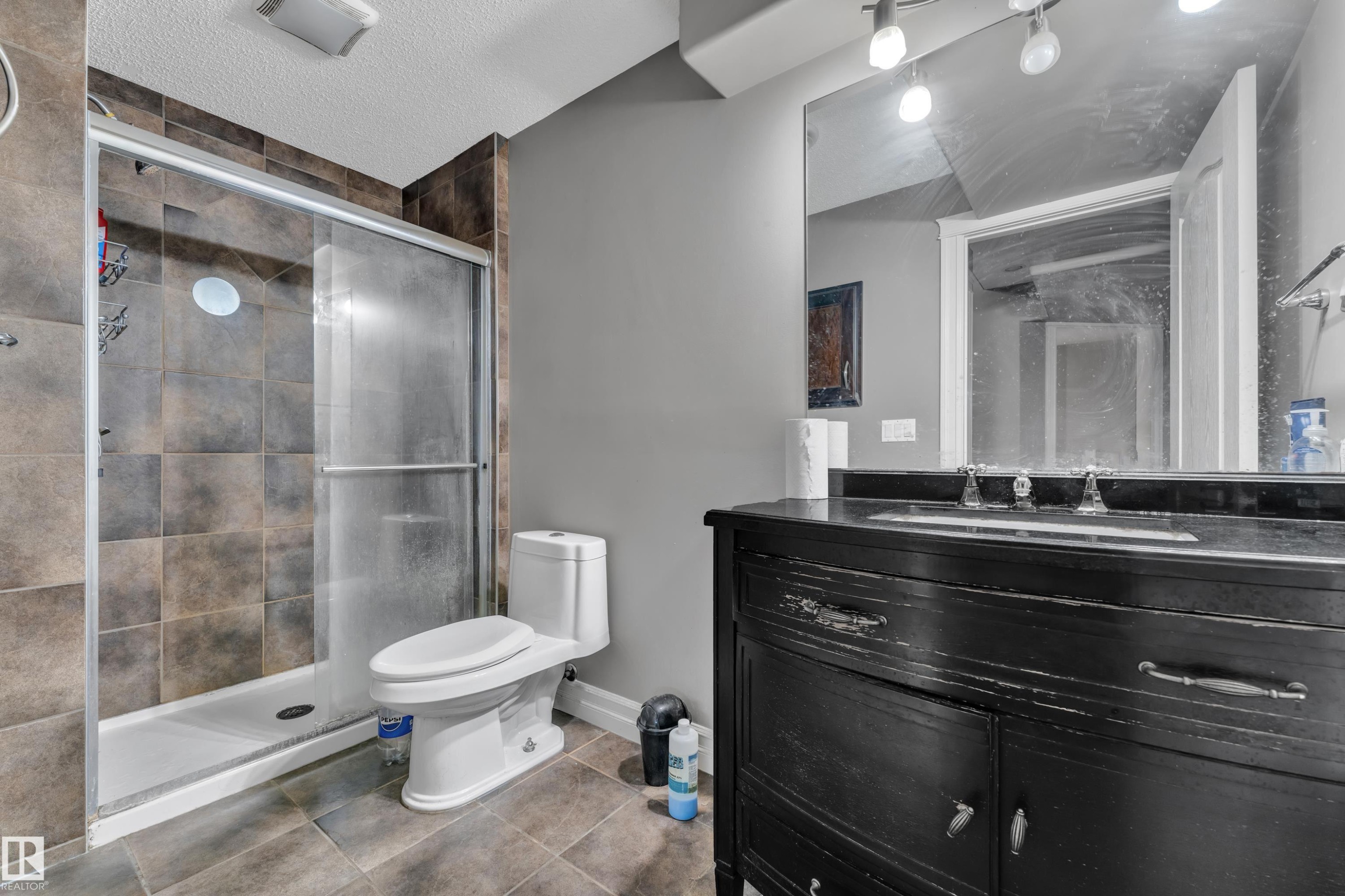 Bathroom featuring a dark wood vanity with dual sinks, a large mirror, and track lighting - 6116 11 Avenue, Edmonton, AB