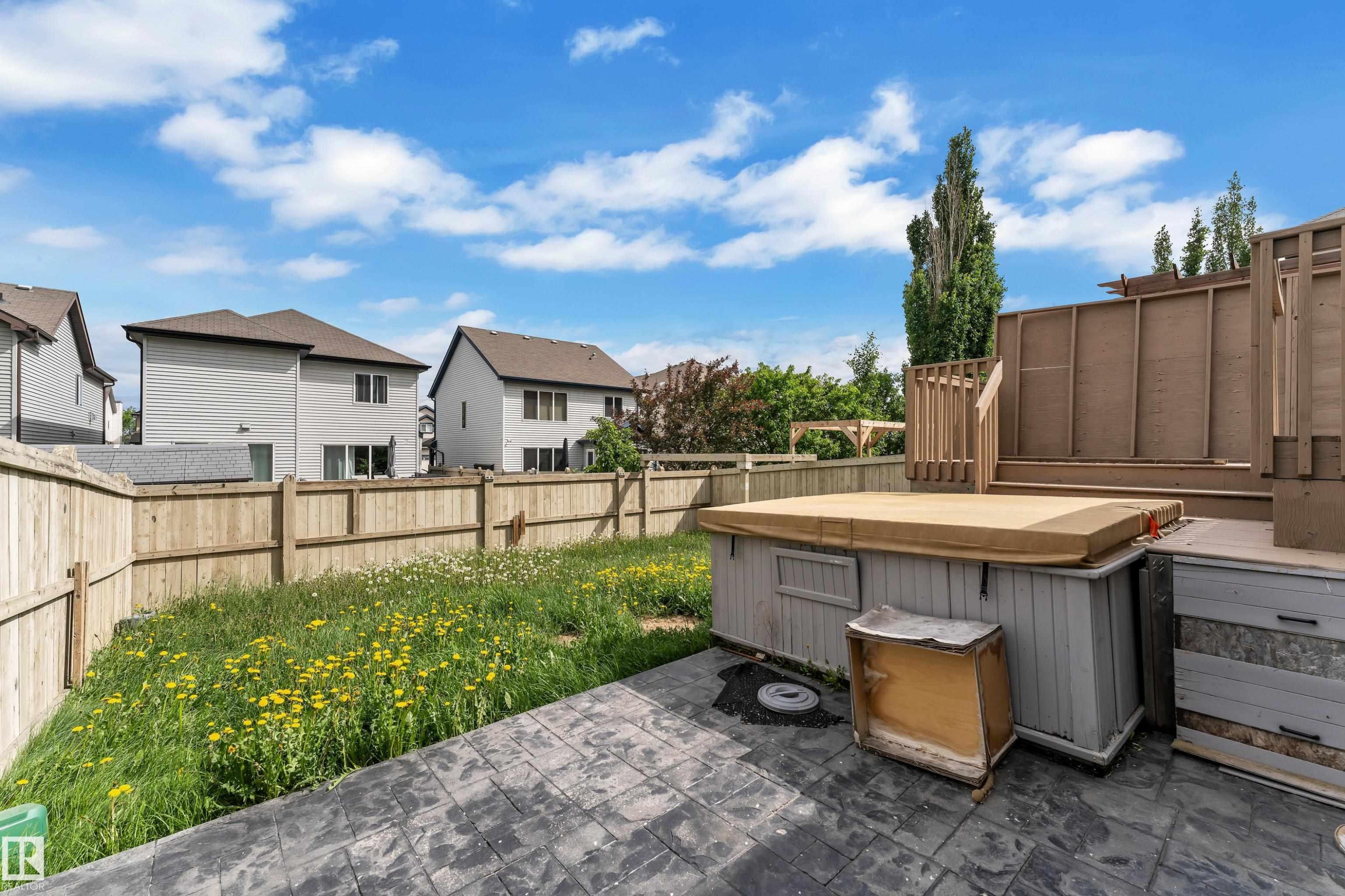 Backyard featuring an imprinted concrete patio, a wooden privacy fence, a raised wood deck, and a hot tub - 6116 11 Avenue, Edmonton, AB