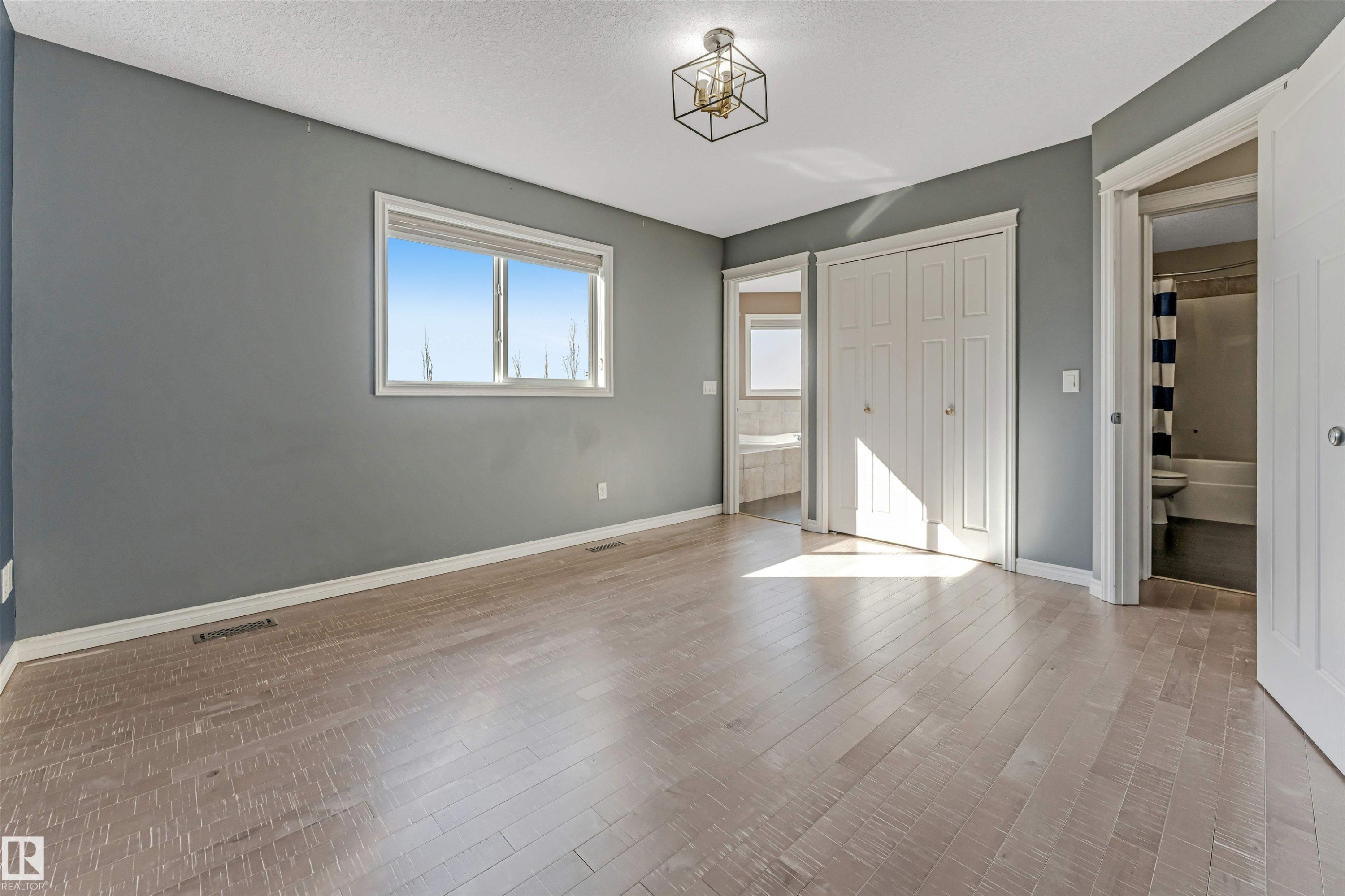 Spacious room featuring light wood-finish flooring, a window with white trim, and a contemporary ceiling light fixture - 5928 12 Avenue, Edmonton, AB