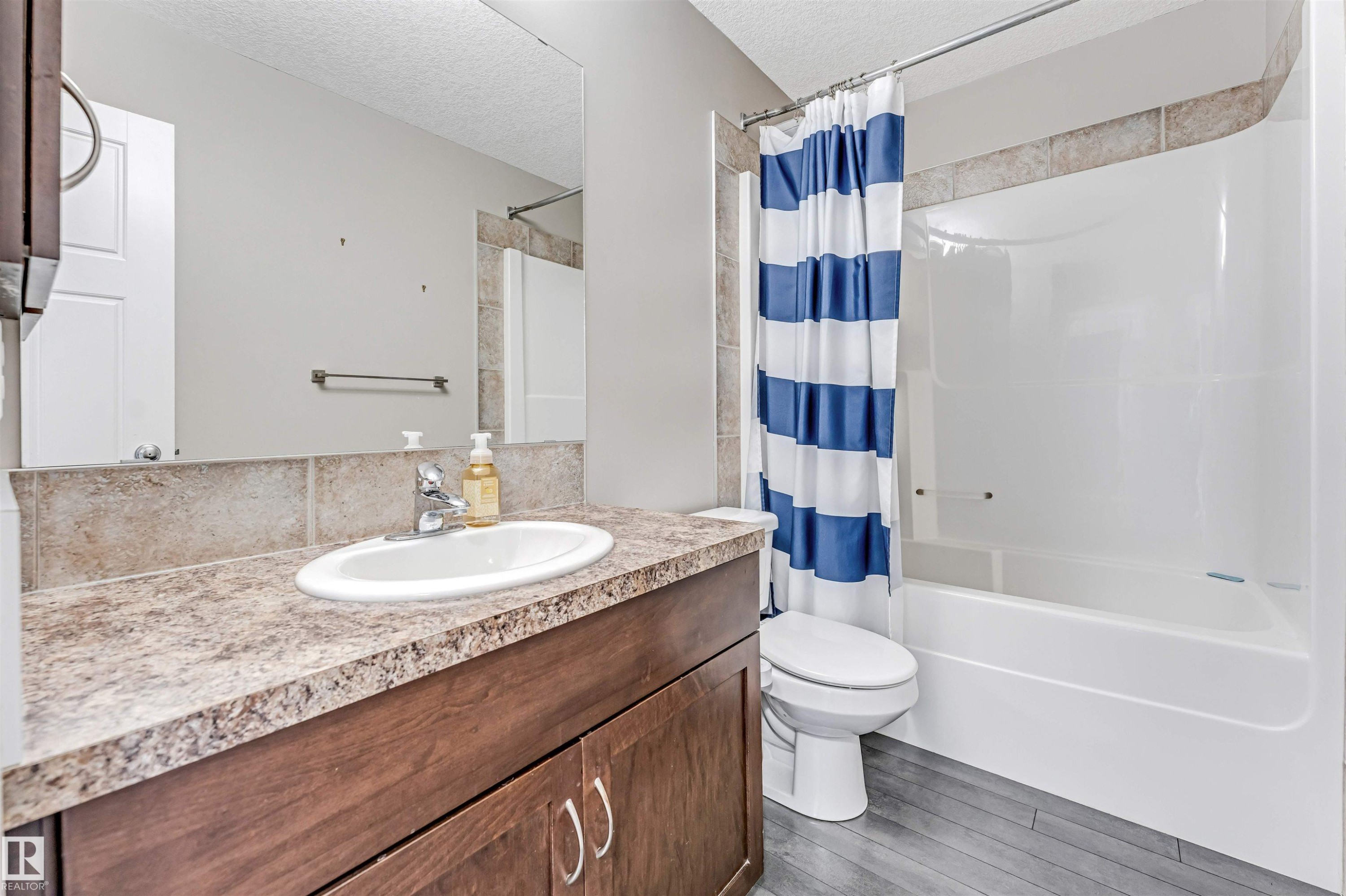 Bathroom featuring a wood-finish vanity with a laminate countertop, an undermount sink, and a large mirror - 5928 12 Avenue, Edmonton, AB