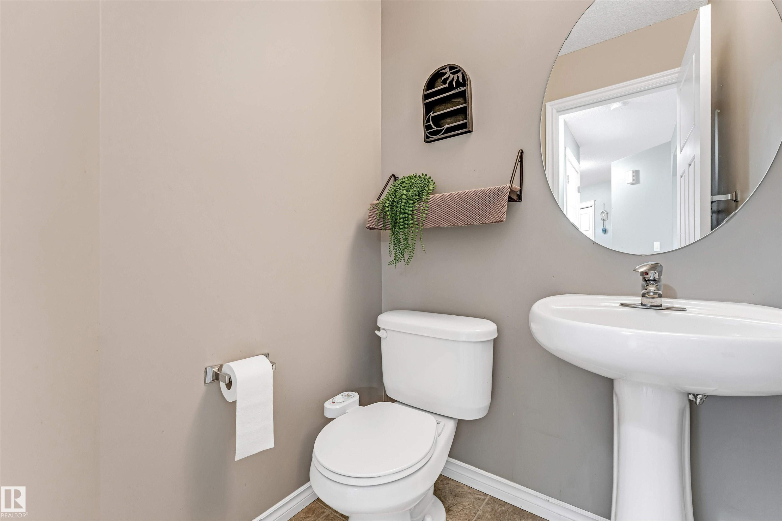 Pedestal sink with chrome faucet hardware, round wall mirror, and neutral wall tones - 5928 12 Avenue, Edmonton, AB