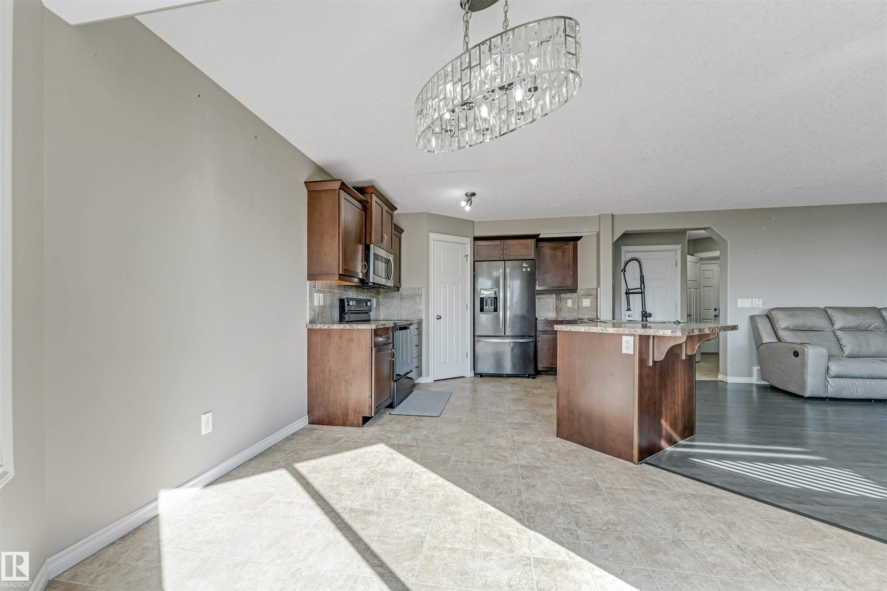 Open-concept kitchen and dining area featuring dark wood cabinetry, stainless steel appliances, granite countertops, and an island with a breakfast bar - 5928 12 Avenue, Edmonton, AB