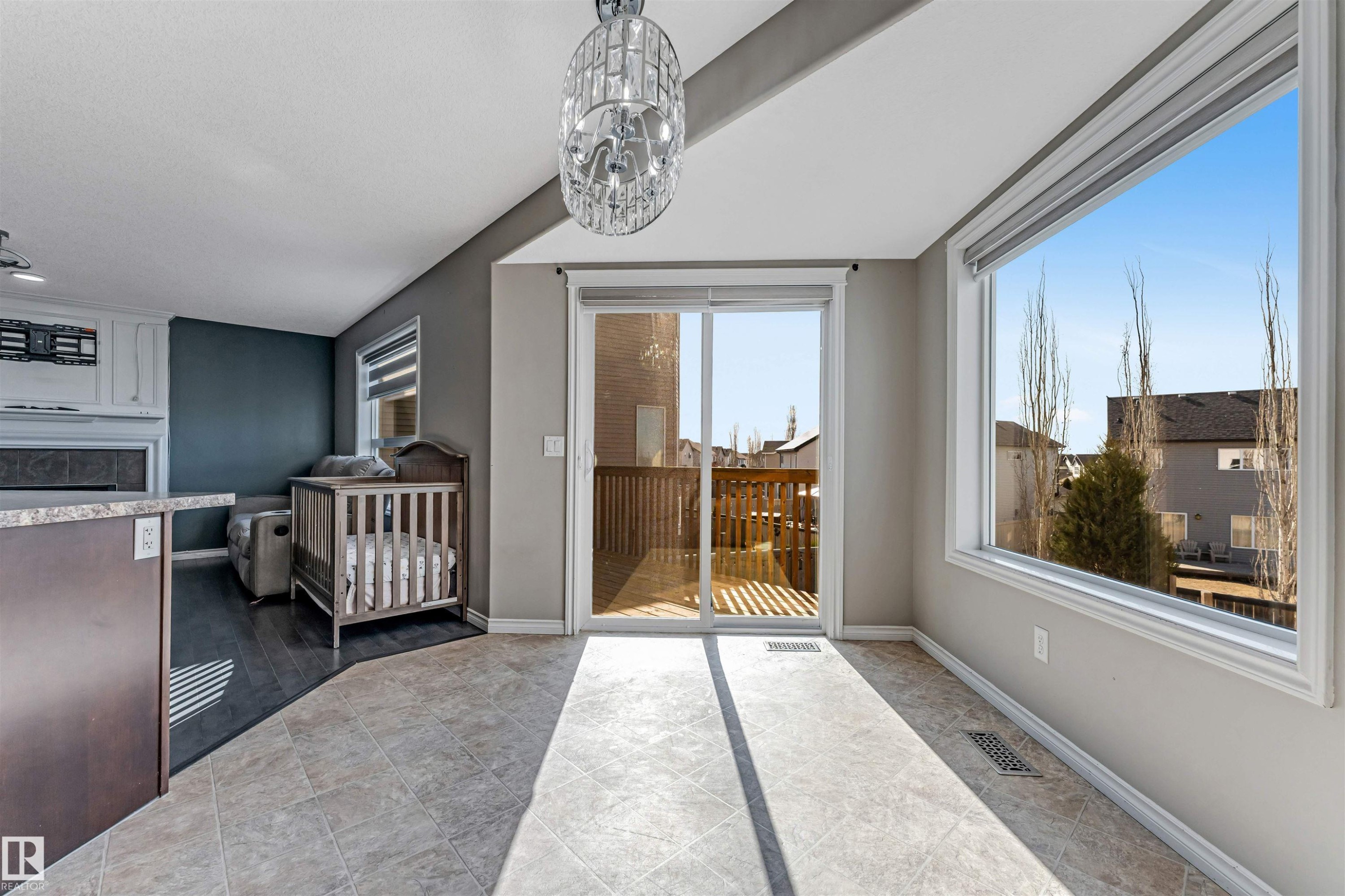 Open-concept room featuring tile flooring, a large picture window, and direct access to an outdoor deck through sliding glass doors - 5928 12 Avenue, Edmonton, AB