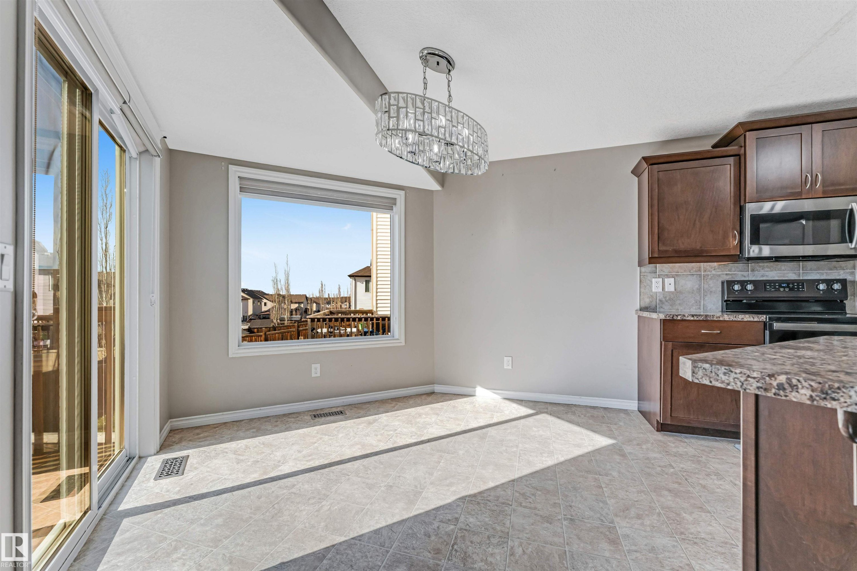 Open-concept dining area featuring a crystal chandelier, tile flooring, and a large window with white trim - 5928 12 Avenue, Edmonton, AB
