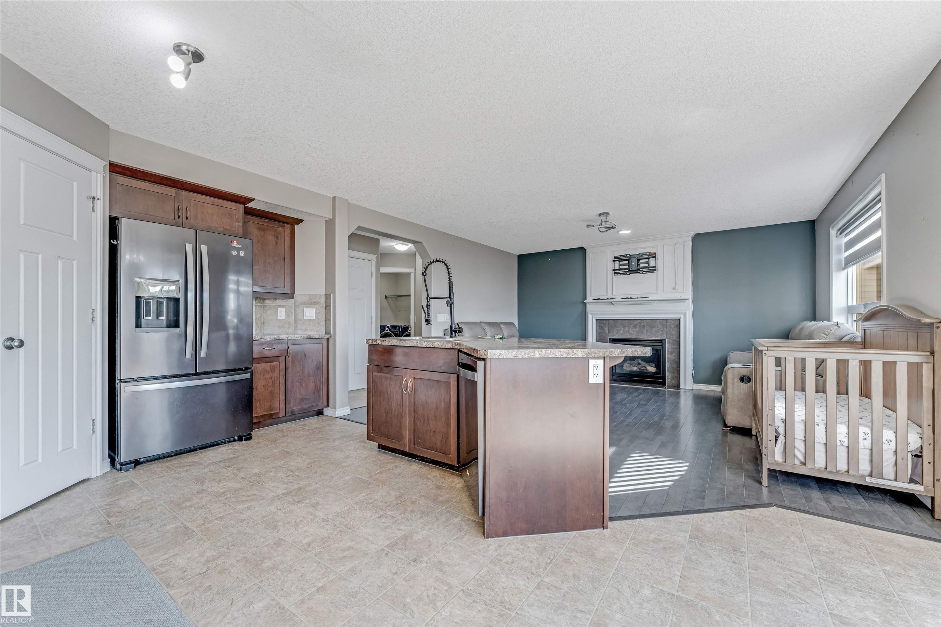 Open-concept living space featuring a kitchen island with stone-finish countertops, stainless steel appliances, and wood cabinetry - 5928 12 Avenue, Edmonton, AB