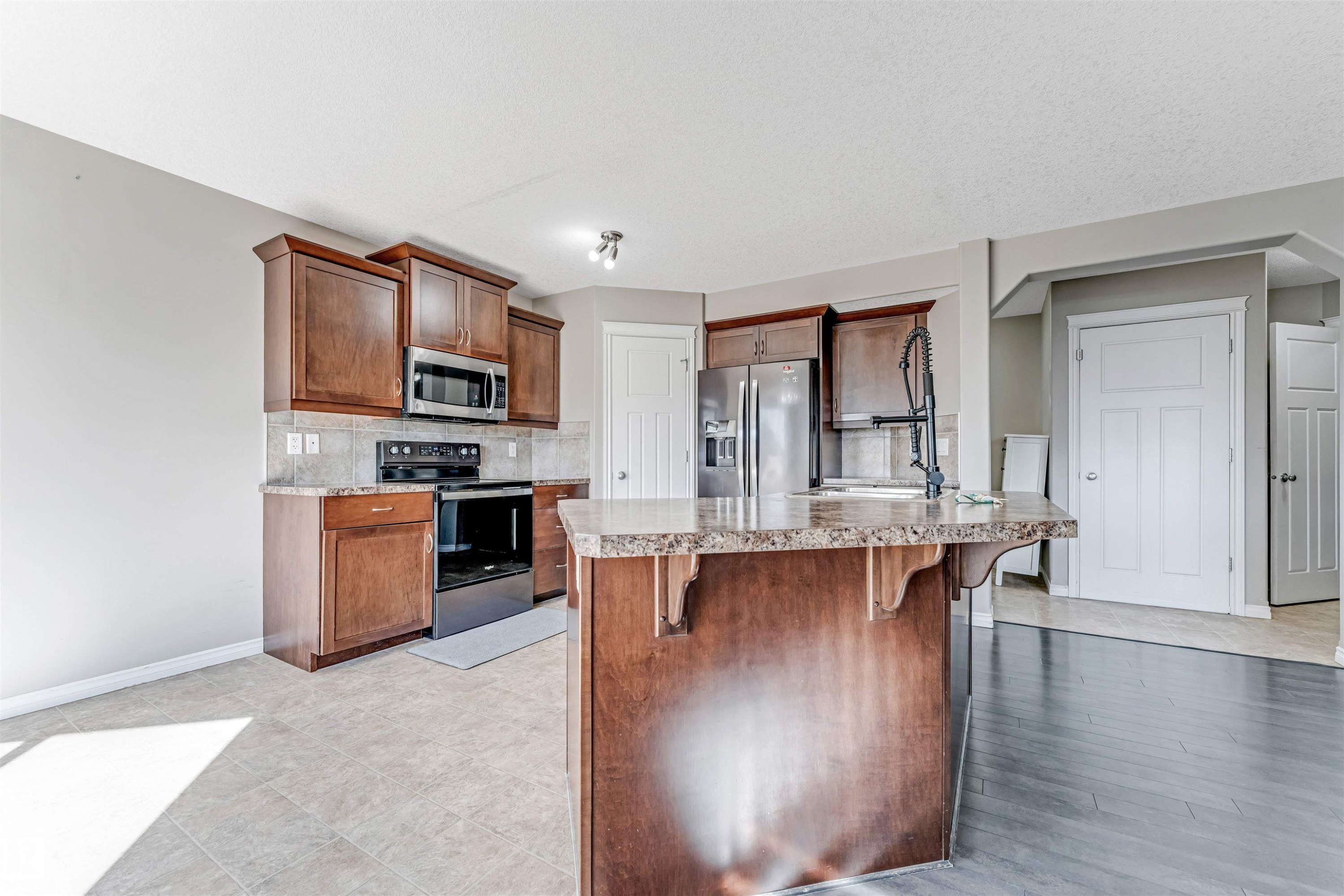 Kitchen featuring dark wood cabinetry, stainless steel appliances, stone-finish countertops, and a central island with an integrated sink - 5928 12 Avenue, Edmonton, AB