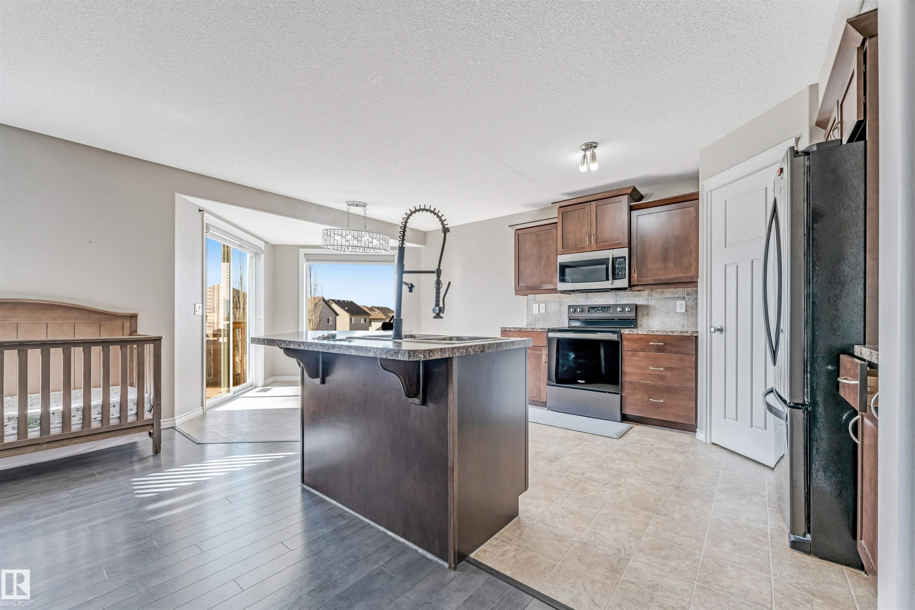 Kitchen featuring a central island with a gooseneck faucet, dark wood cabinetry, stainless steel appliances, and tile flooring - 5928 12 Avenue, Edmonton, AB