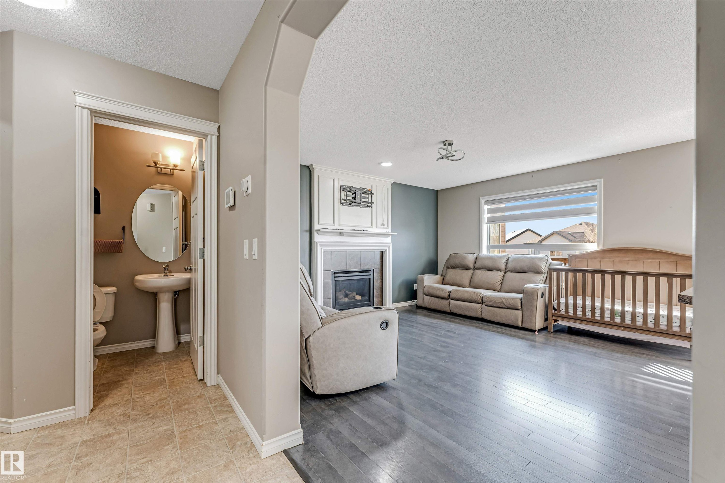 Living area with dark wood-finish flooring and a fireplace featuring a white mantel and tile surround - 5928 12 Avenue, Edmonton, AB