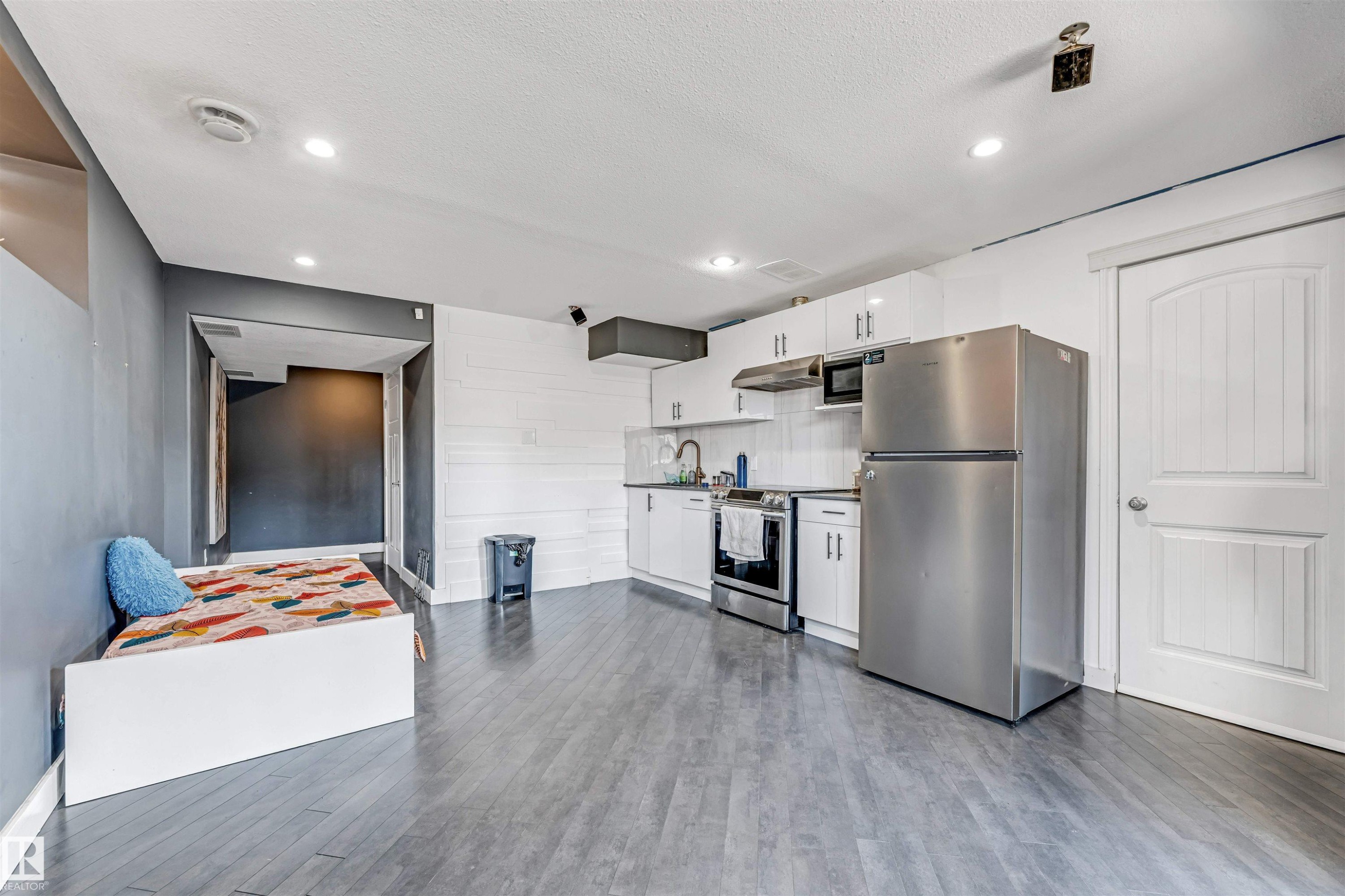 Contemporary kitchen area featuring stainless steel appliances, white cabinetry, and wood-finish flooring - 5928 12 Avenue, Edmonton, AB