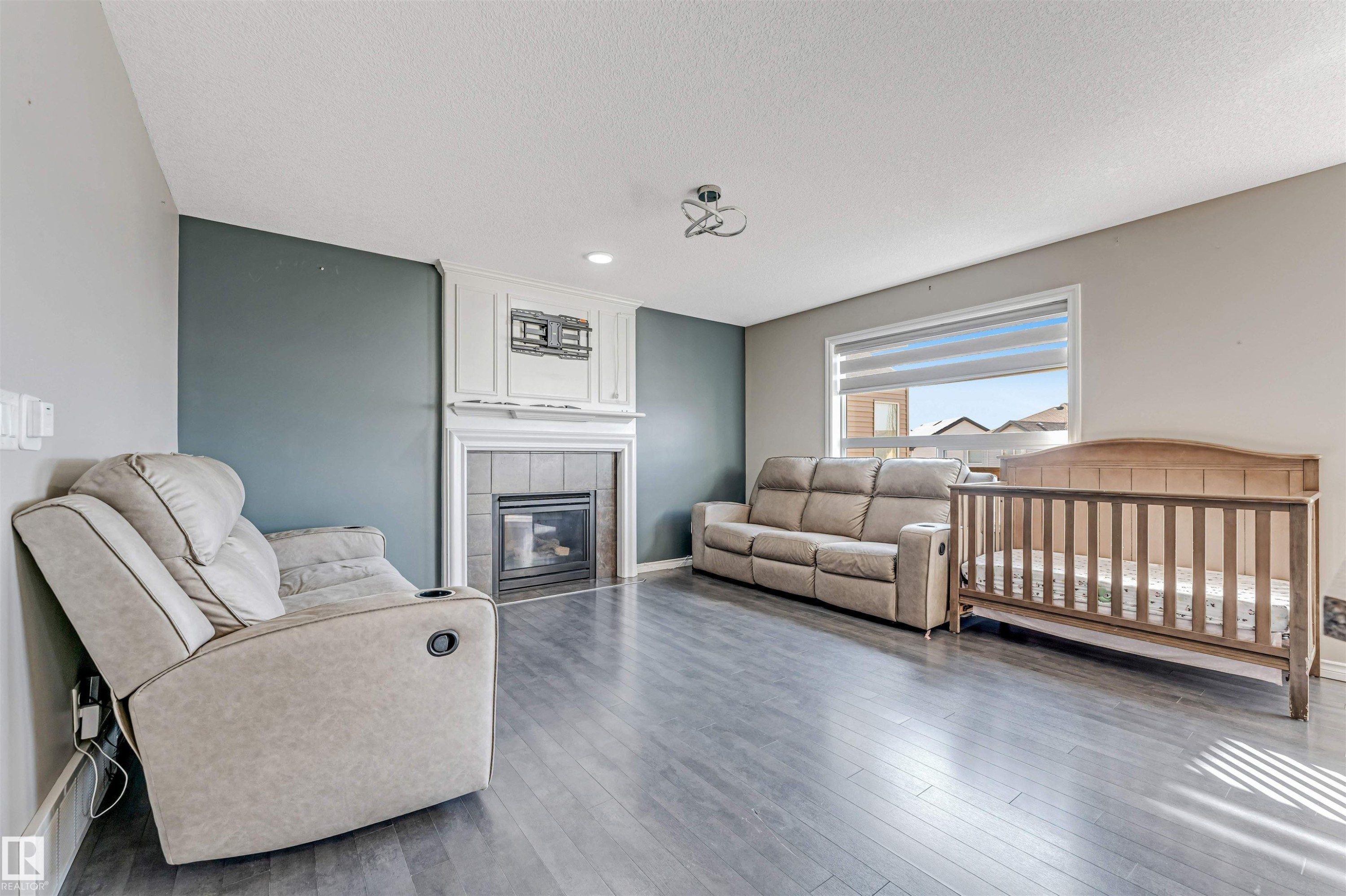 Living area featuring wood-finish flooring, a contemporary ceiling light fixture, and a fireplace with a white mantel and tile surround - 5928 12 Avenue, Edmonton, AB