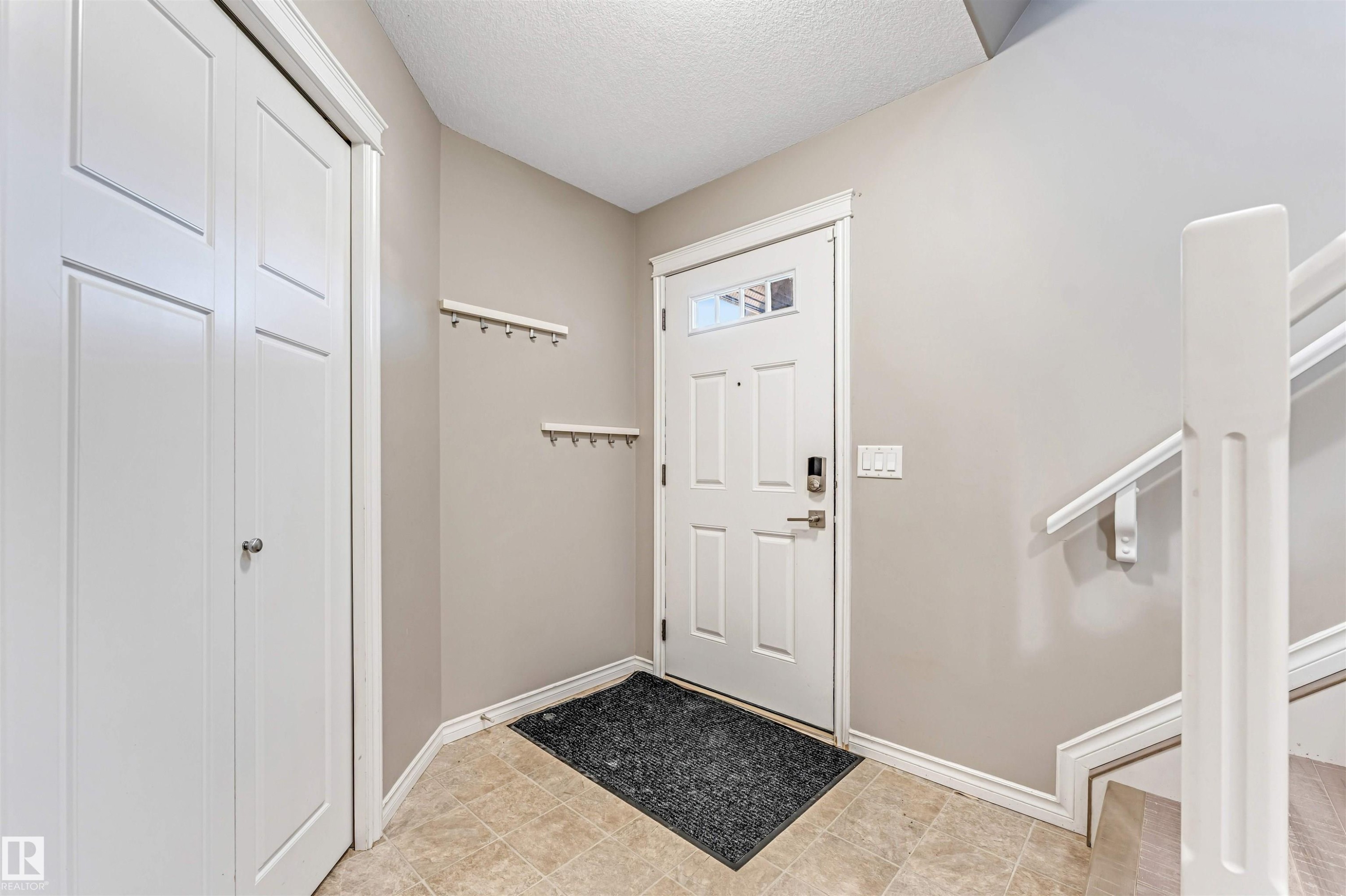 Entryway featuring neutral wall tones, ceramic tile flooring, a paneled front door with decorative glass inserts, and a built-in closet with bi-fold doors - 5928 12 Avenue, Edmonton, AB