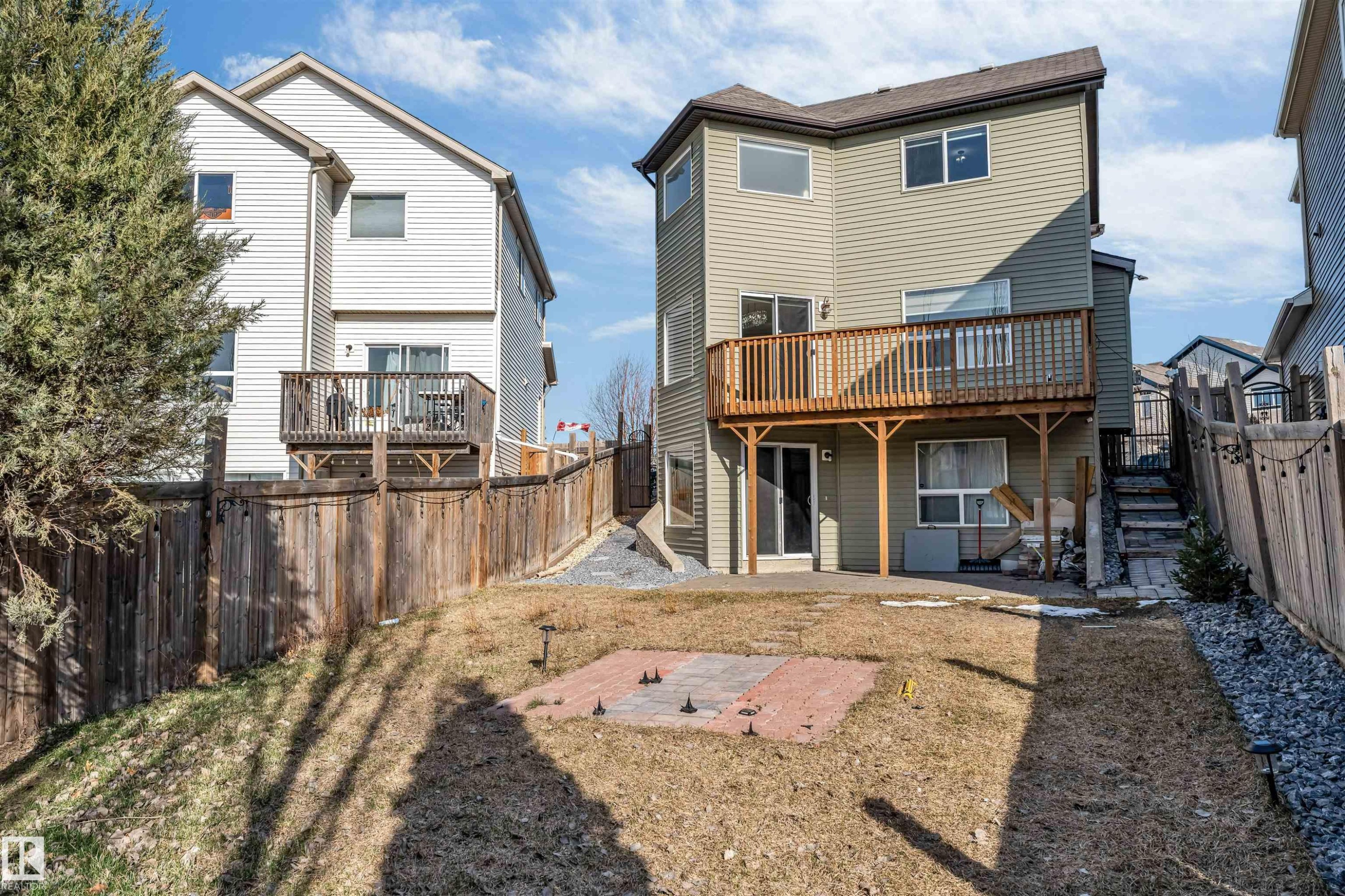 Expansive backyard featuring a multi-level wooden deck, ground-level patio access, and a paved brick area - 5928 12 Avenue, Edmonton, AB