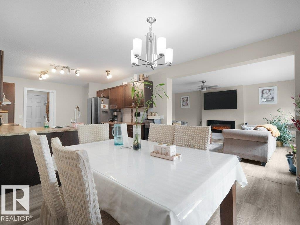 Dining area featuring a modern chandelier, wood-finish flooring, and direct sightlines to the living area with a fireplace and the kitchen with track lighting - 3756 8 Street, Edmonton, AB