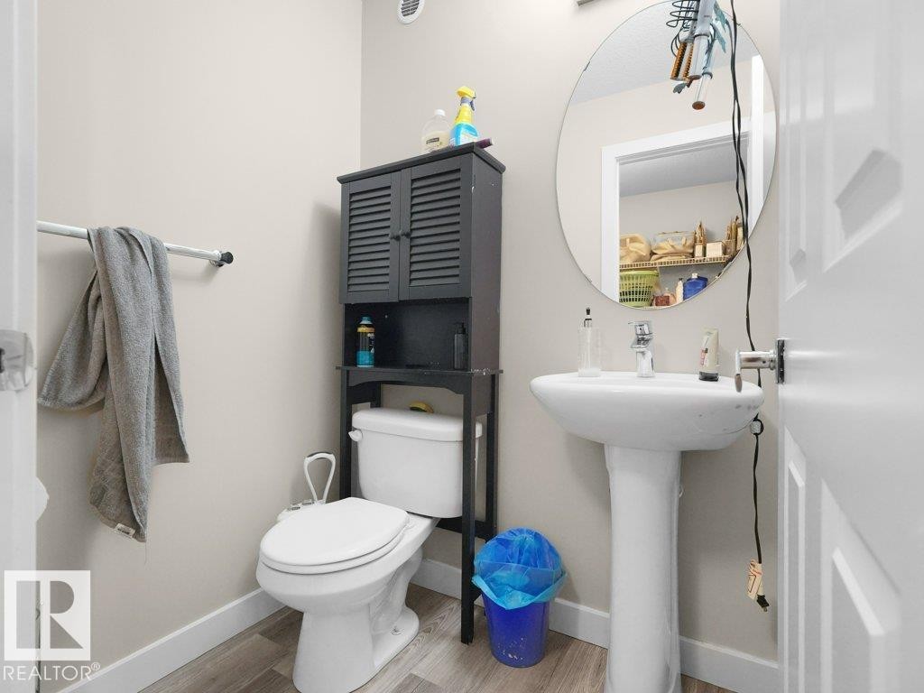 Bathroom featuring a white pedestal sink, circular wall-mounted mirror, and wood-finish flooring - 3756 8 Street, Edmonton, AB