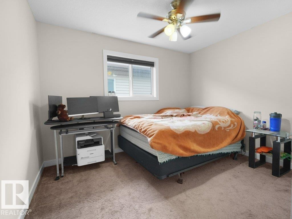 Carpeted room featuring a ceiling fan with integrated lighting, a window with horizontal blinds, and neutral wall paint - 3756 8 Street, Edmonton, AB