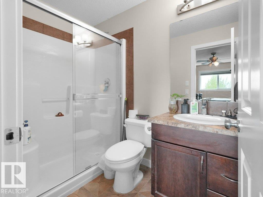 Full bathroom featuring a shower with a sliding glass enclosure, a white toilet, and a vanity with a dark wood-finish cabinet and a light-colored countertop - 3756 8 Street, Edmonton, AB