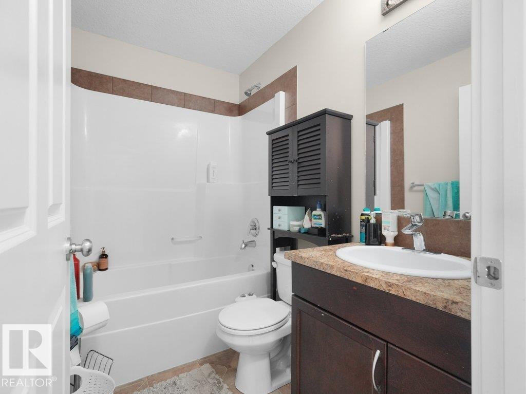 Bathroom featuring a white bathtub and shower combination, brown accent tile, a dark wood-finish vanity with a single sink, and a framed mirror - 3756 8 Street, Edmonton, AB
