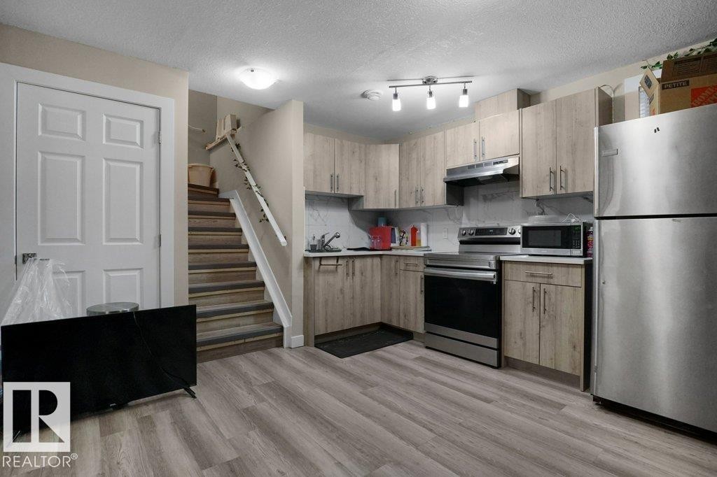 Kitchen area featuring wood-finish cabinetry, stainless steel appliances, laminate wood-look flooring, and a track lighting fixture - 3756 8 Street, Edmonton, AB