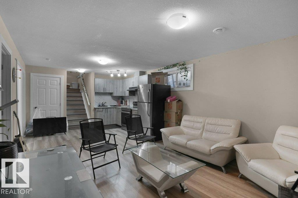 Open-concept living space featuring wood-finish flooring, a contemporary kitchen with stainless steel appliances, light gray cabinetry, and a subway tile backsplash - 3756 8 Street, Edmonton, AB