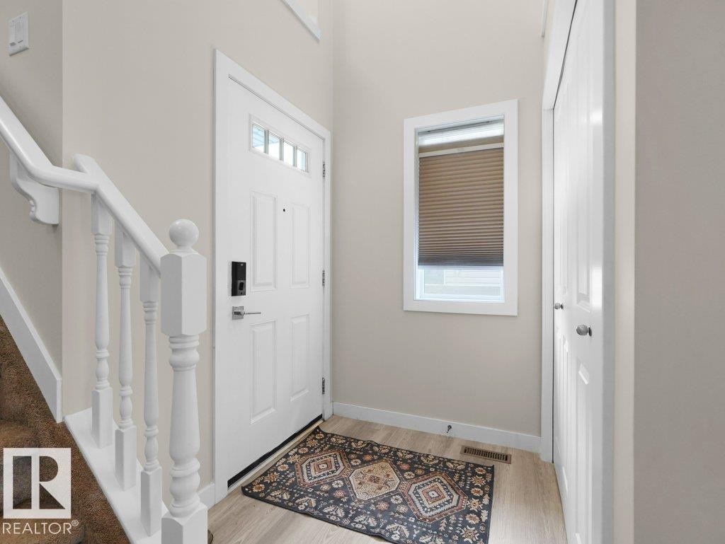 Bright entryway featuring a white paneled door with glass inserts and smart lock, a white staircase with balusters, light wood-finish flooring, and a compact window with blinds - 3756 8 Street, Edmonton, AB