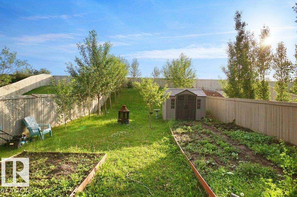 Expansive backyard featuring a lush lawn, multiple mature trees, a dedicated garden bed, a raised garden planter, and a storage shed - 3756 8 Street, Edmonton, AB