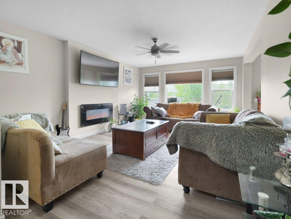 Spacious living area featuring wood-finish flooring, an electric fireplace, and multiple windows with roller blinds - 3756 8 Street, Edmonton, AB