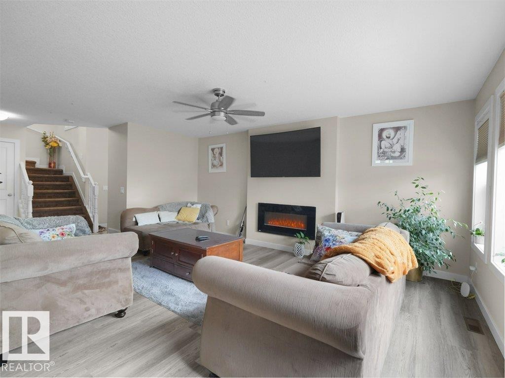 Open-concept living space featuring wood-finish flooring, a contemporary wall-mounted electric fireplace, and a ceiling fan with integrated lighting - 3756 8 Street, Edmonton, AB