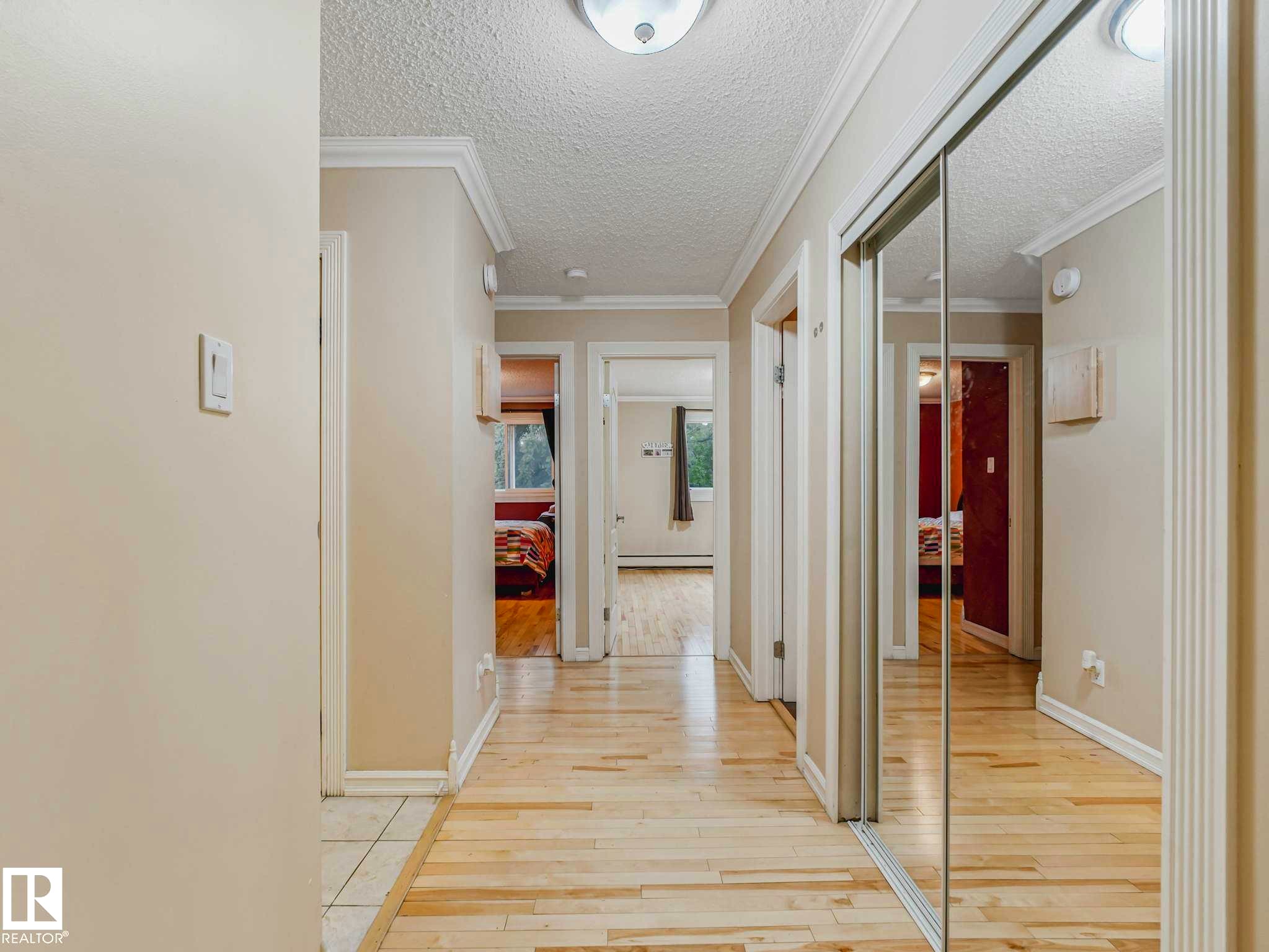 Hallway featuring light wood-finish flooring, white baseboards, and crown molding - #403 10165 113 St Nw, Edmonton, AB