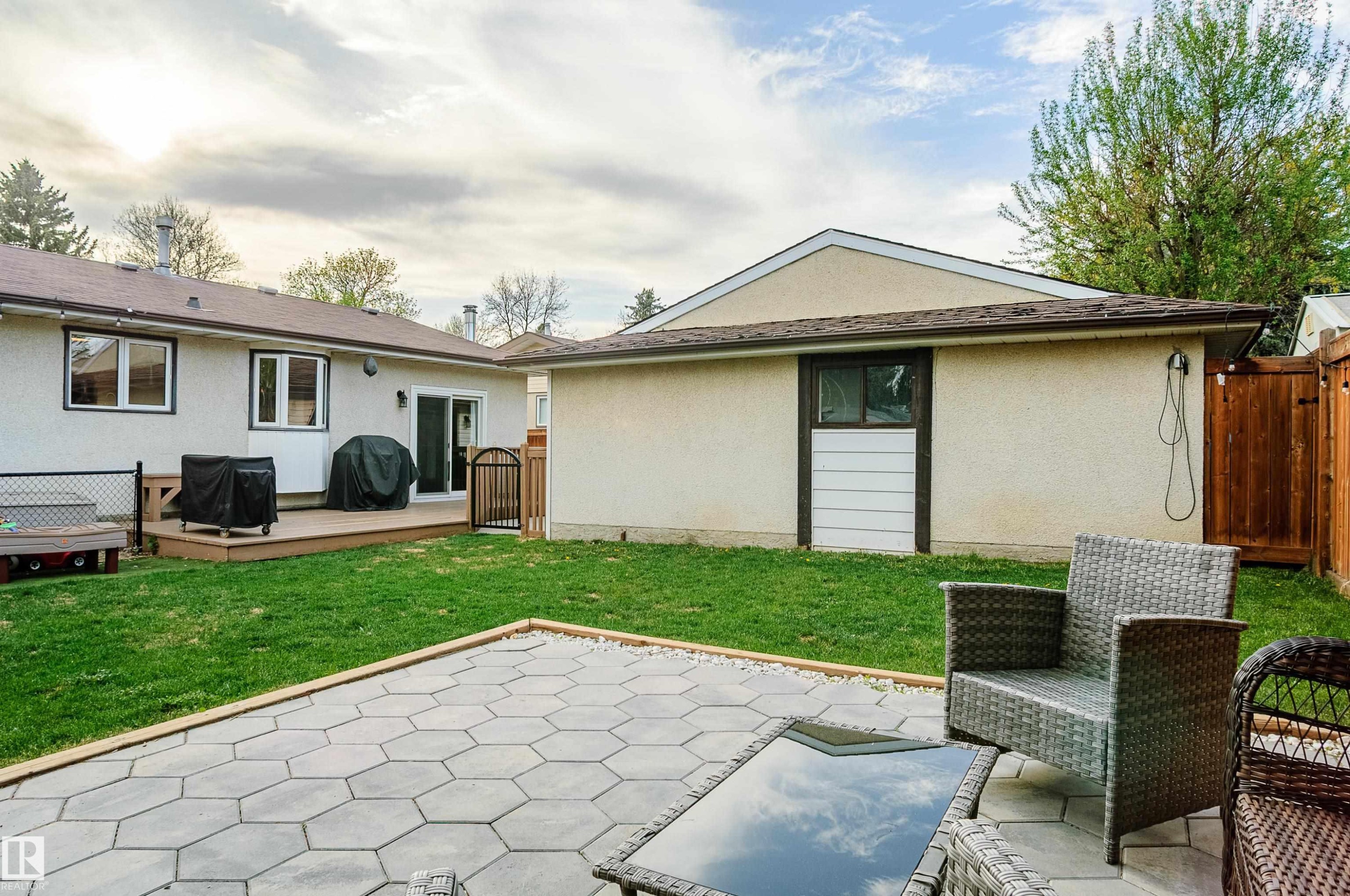 Expansive backyard featuring a hexagonal paver patio, manicured lawn, and a wooden deck - 58 Lodgepole Crescent, St. Albert, AB