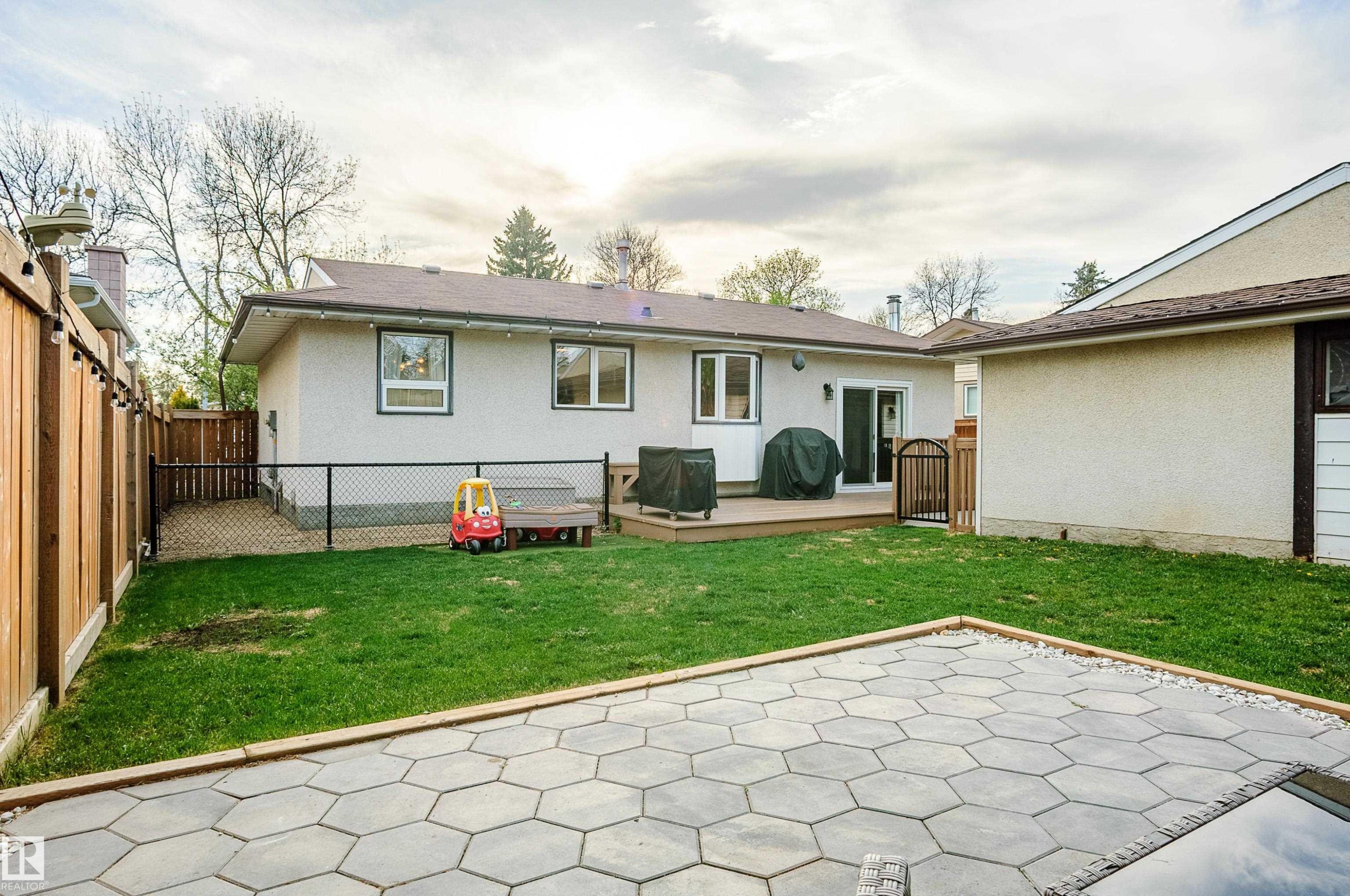 Spacious backyard featuring a vibrant lawn, a hexagonal paver patio, a wooden deck, and a privacy fence - 58 Lodgepole Crescent, St. Albert, AB