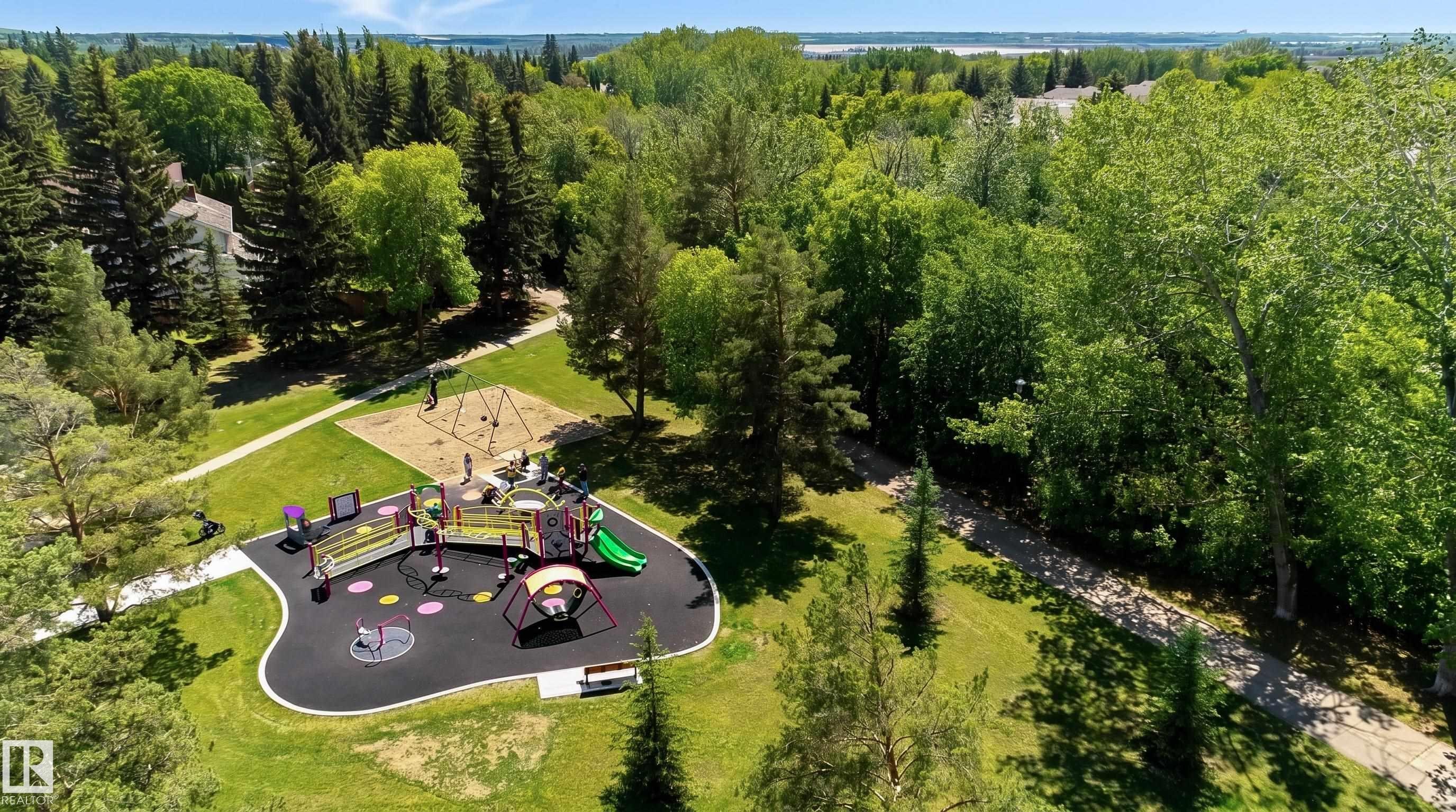 Expansive park area featuring a modern playground with soft-fall surfacing, a swing set on sand, mature trees, and paved walking paths - 58 Lodgepole Crescent, St. Albert, AB